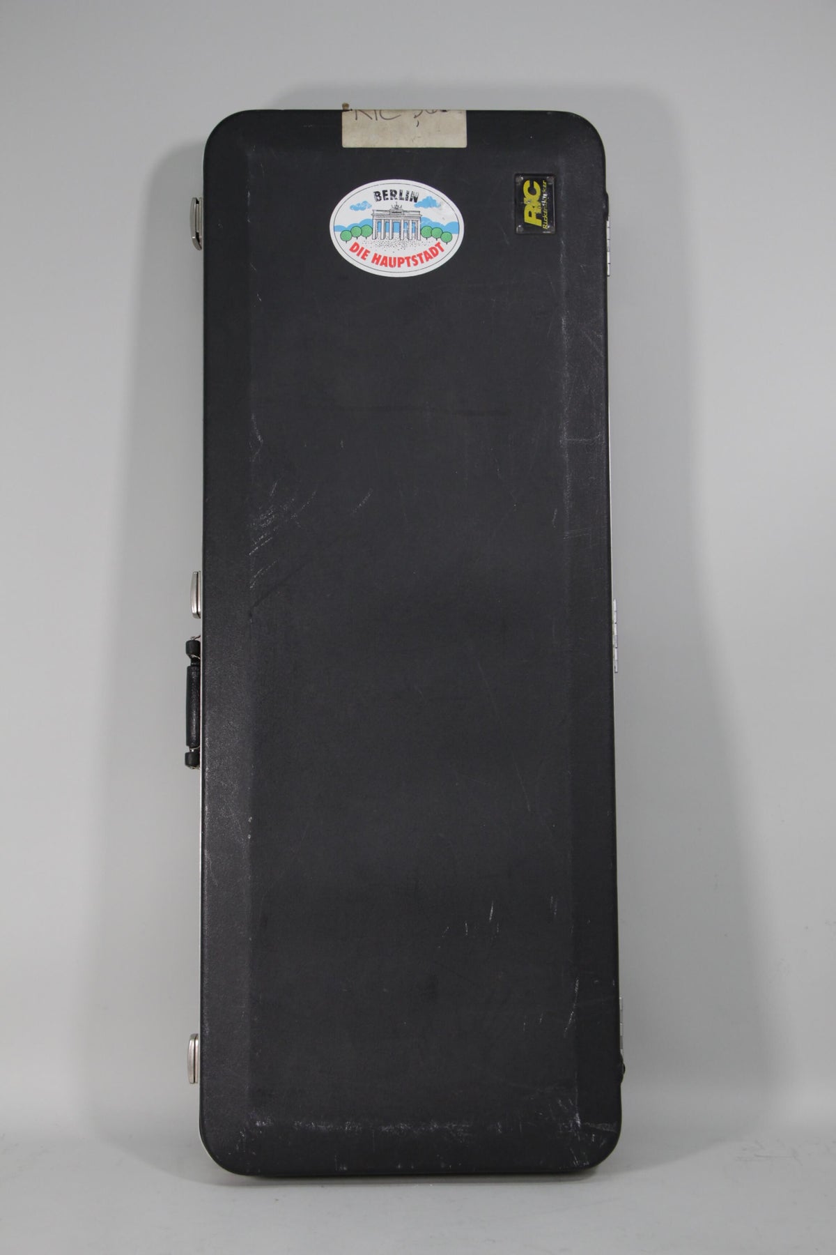 Black hard case with a "Berlin Die Hauptstadt" sticker, a small yellow "RIC" sticker, and visible scuffs and wear.