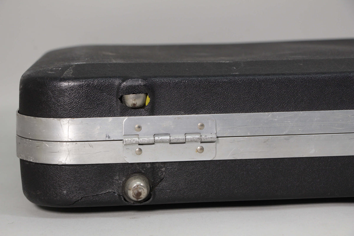 Close-up of the black hard shell case's side, showing a silver hinge, scuffs, and a crack near a metal foot.