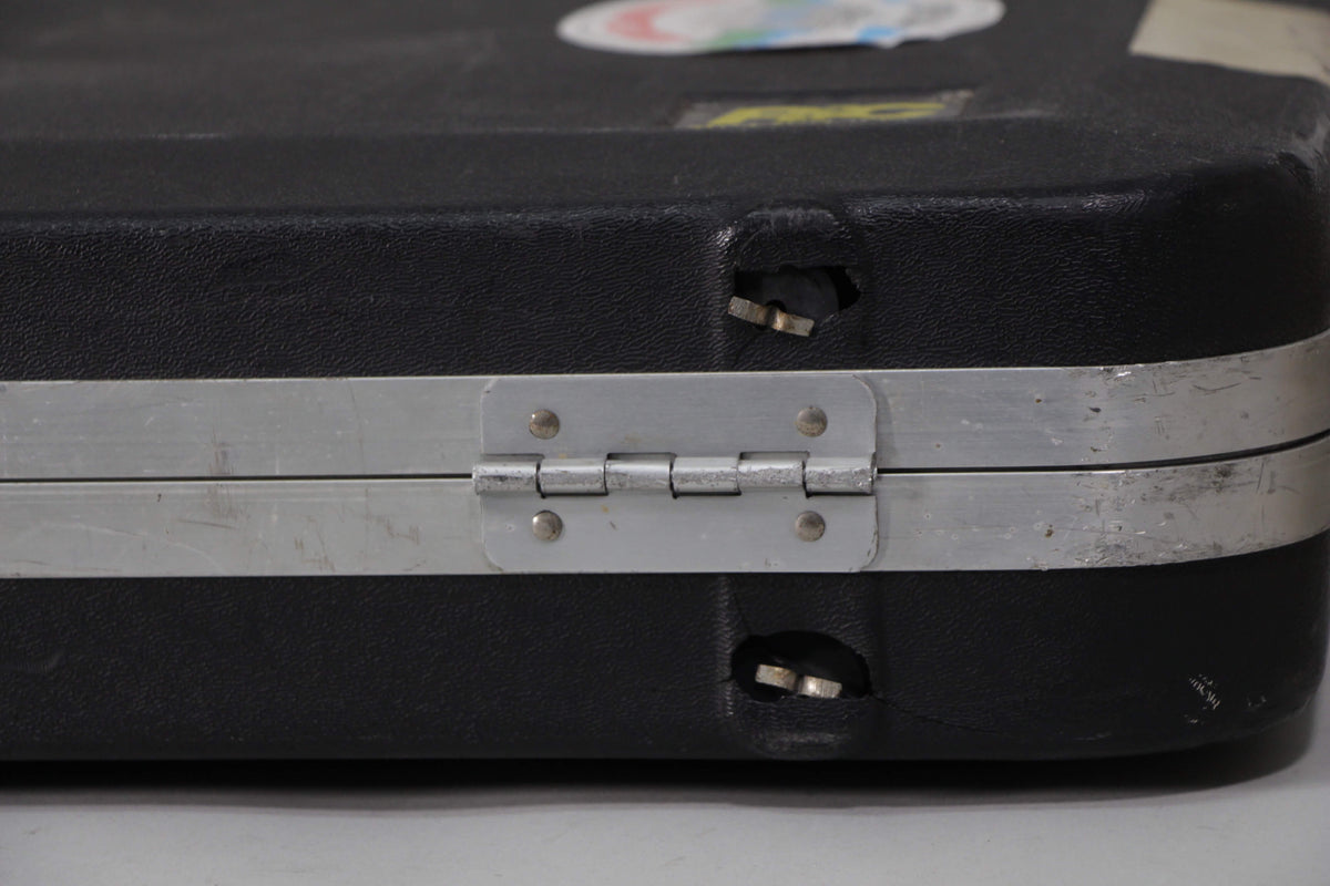 Close-up of the black hard shell case's metal hinge and two broken latches, showing wear and tear on the case.
