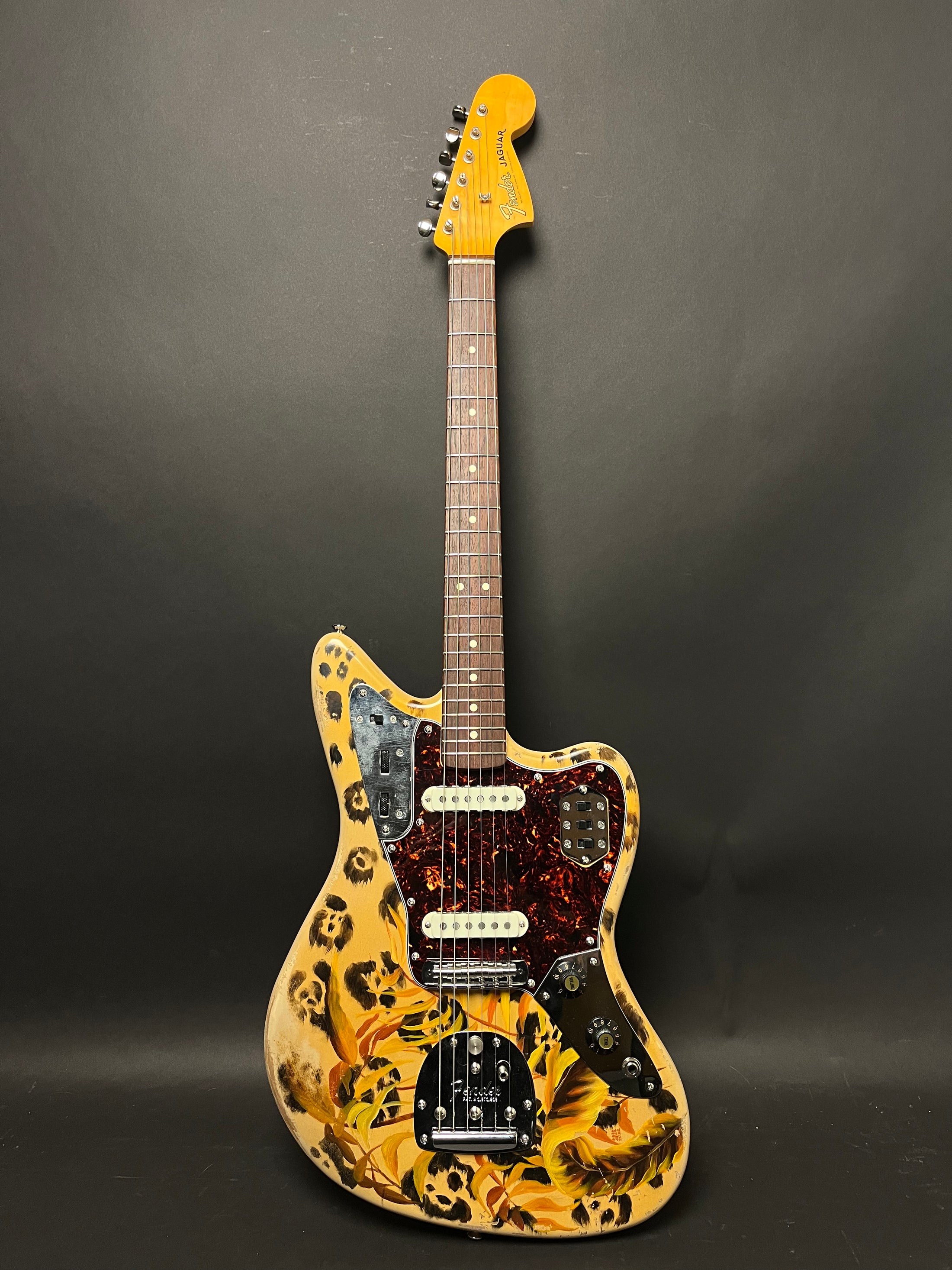 Full-body view of a cream Jaguar guitar with leopard spots and yellow flowers, a tortoiseshell pickguard, and chrome hardware.