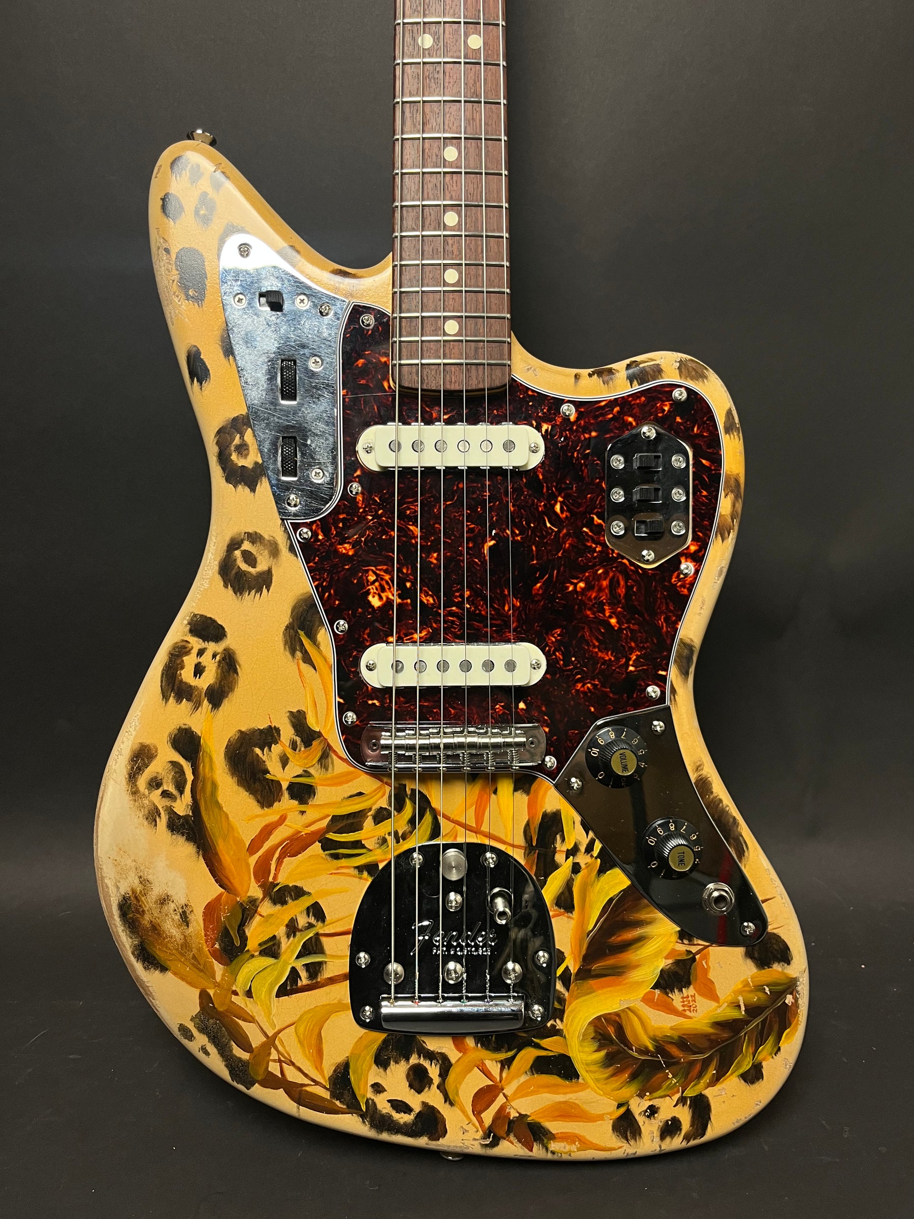 The guitar's body, painted with leopard spots and yellow-orange leaves, is angled slightly, showing the neck, pickups, and controls.