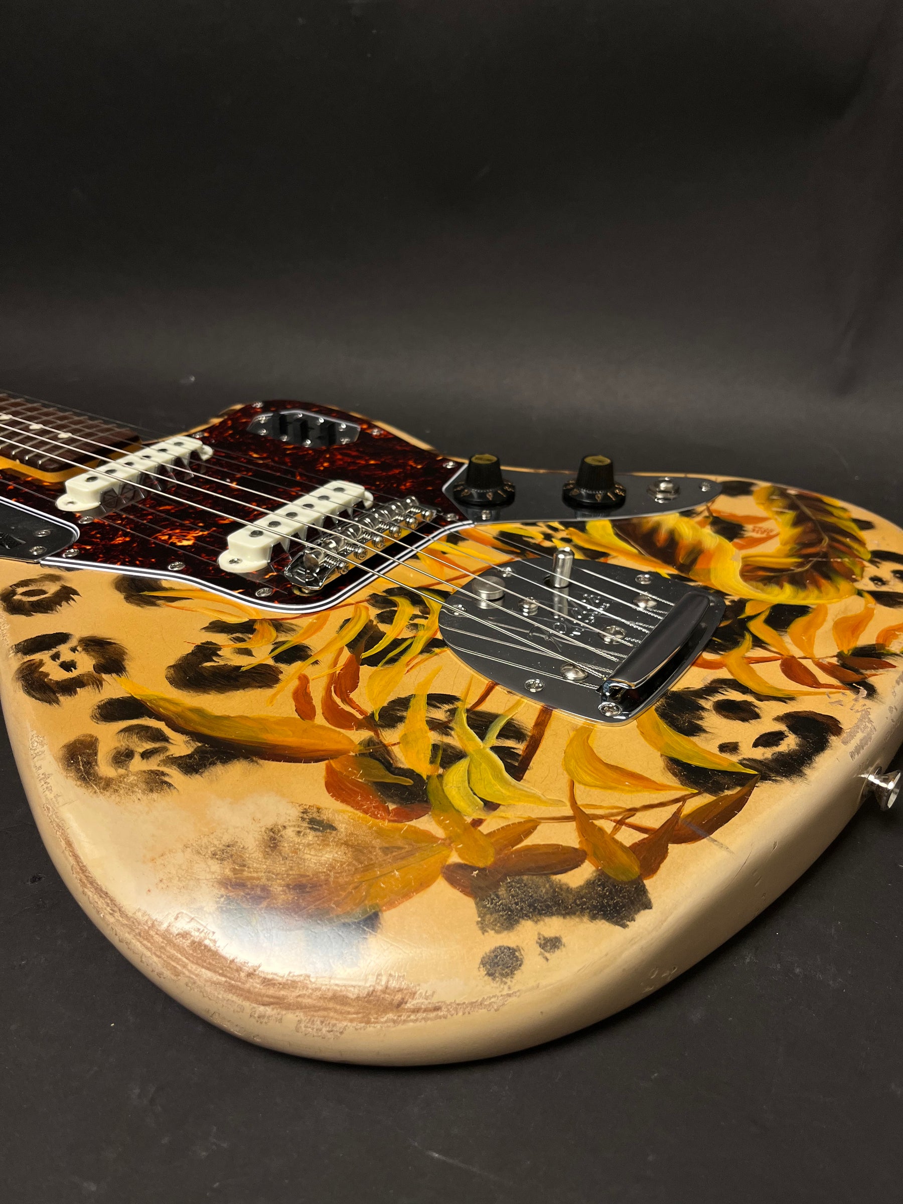 The guitar body, angled right, shows a leopard print and yellow/orange leaves over a distressed cream finish.