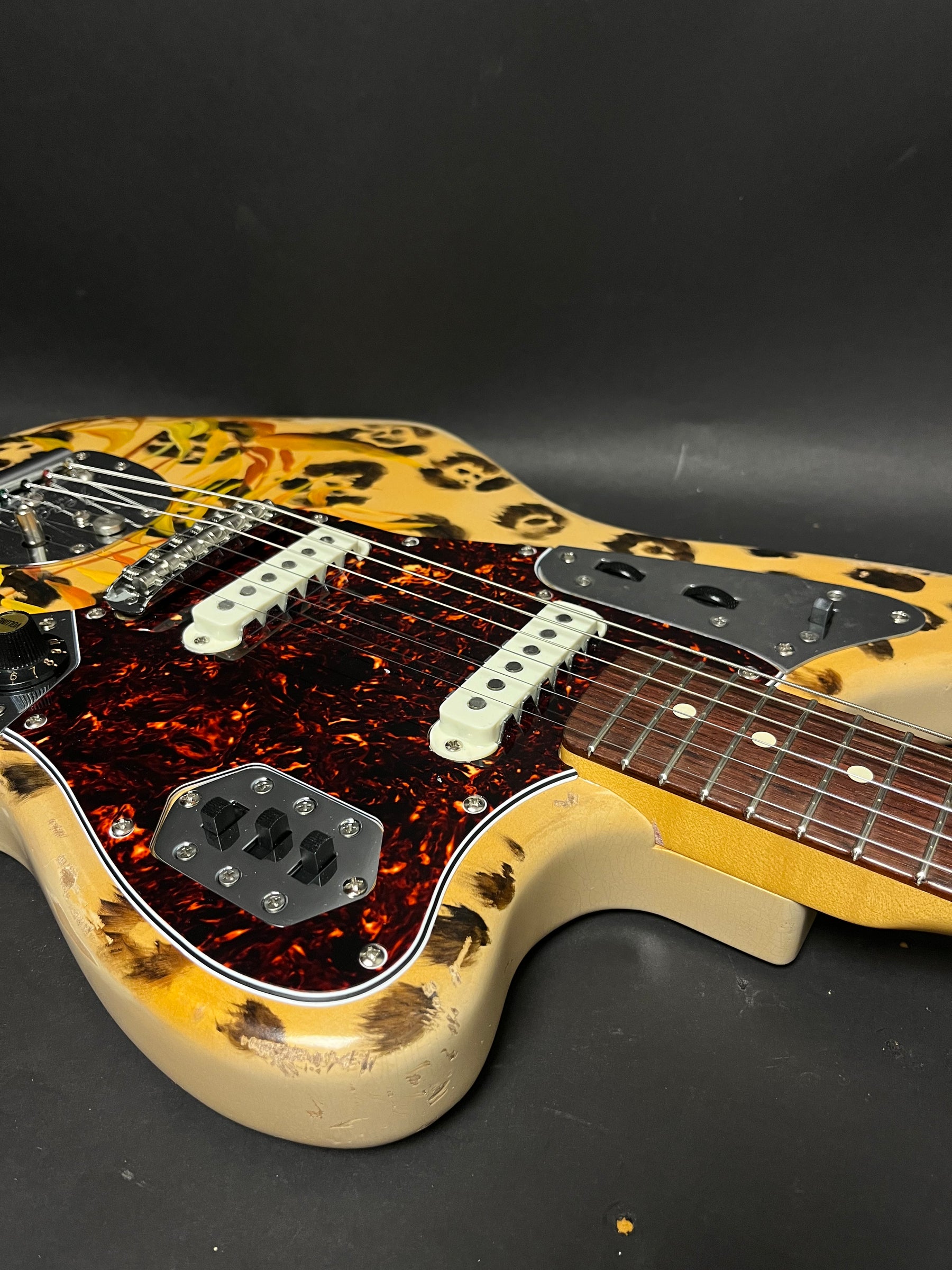 Close-up of the guitar body, showing the leopard print finish, tortoiseshell pickguard, white pickups, and heavy relic wear on the lower bout.