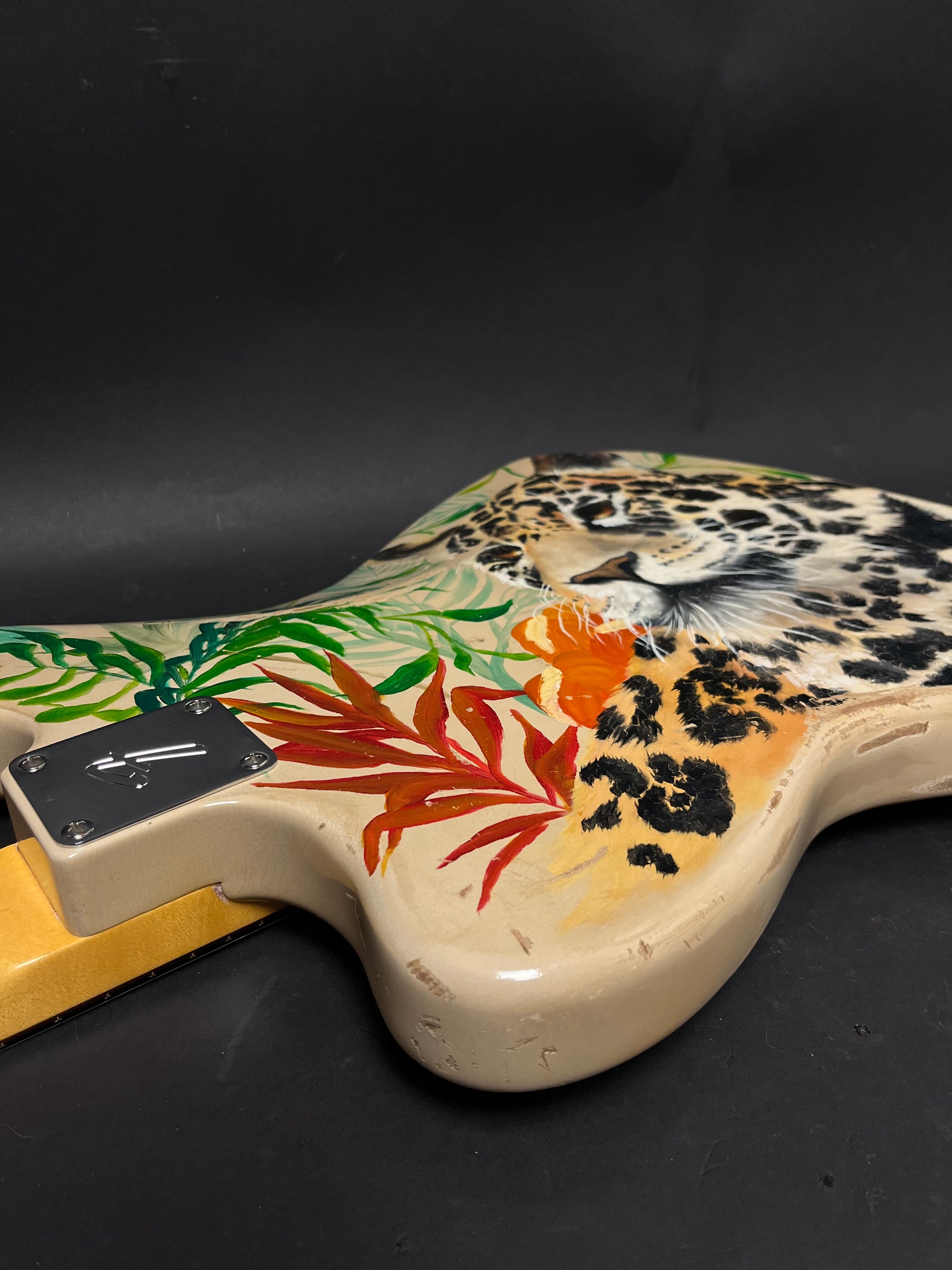 The guitar body, painted with a jaguar head and tropical leaves, shows visible wear and checking on its cream finish.