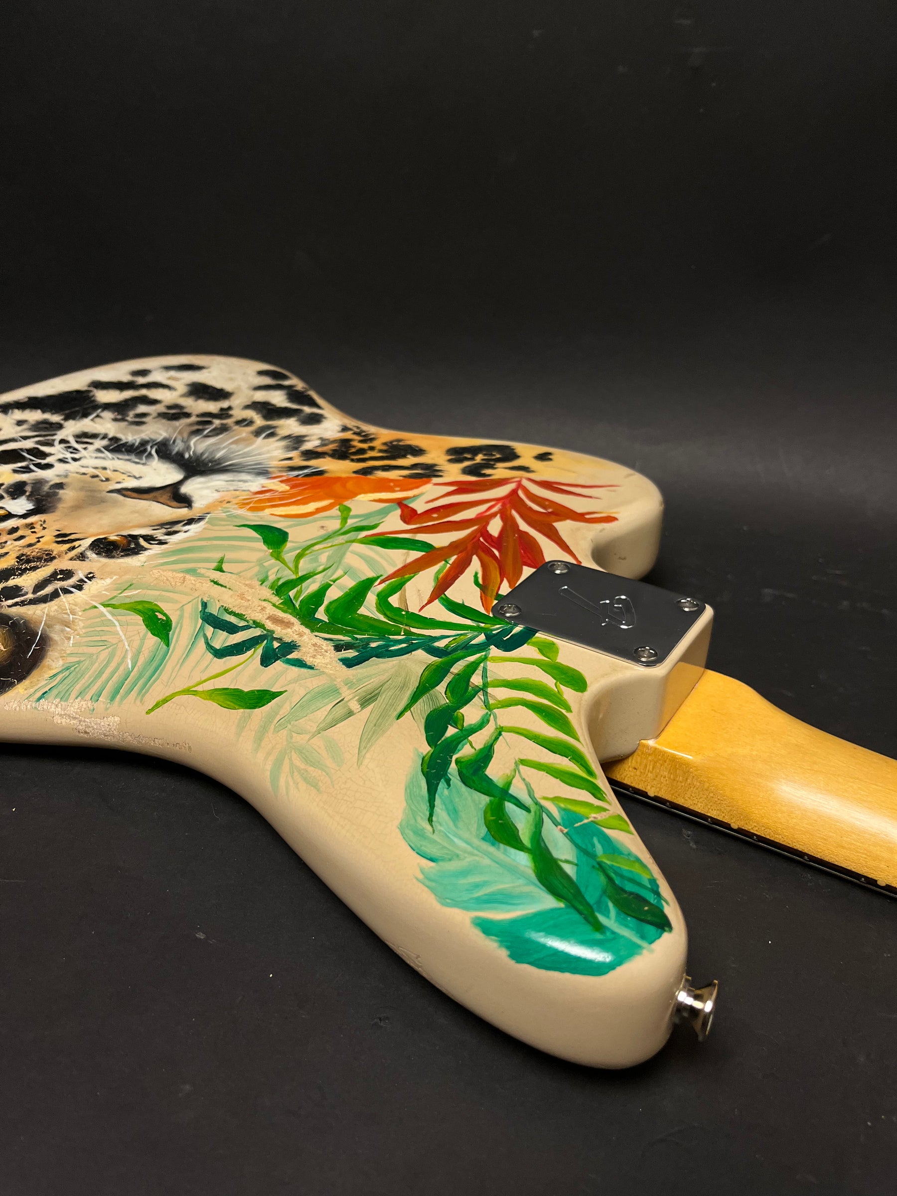 The guitar body's back, painted with a leopard and tropical leaves, shows a large scratch and neck plate.