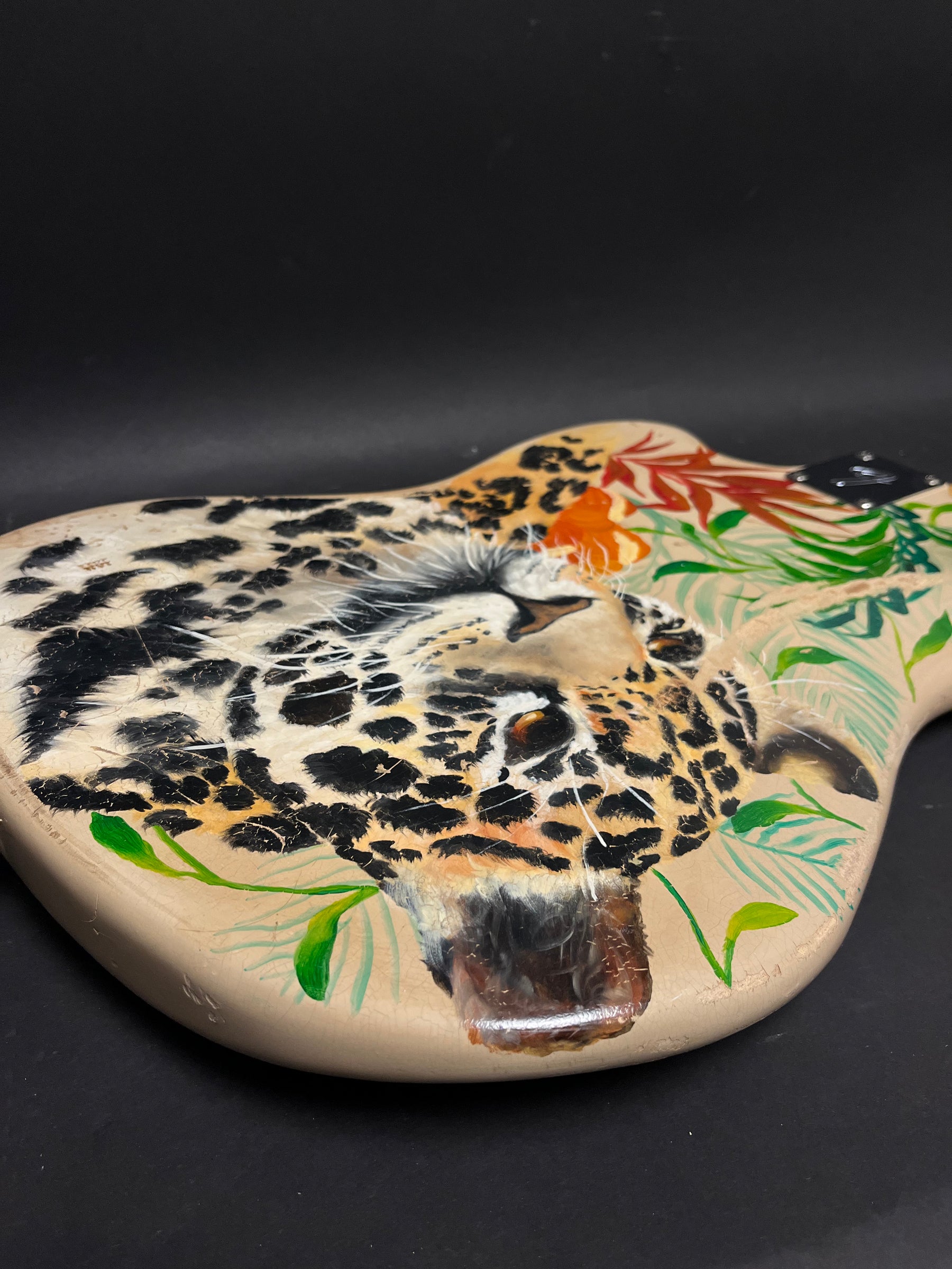 Close-up of the guitar body, showing a hand-painted jaguar head with tropical leaves and visible finish checking.