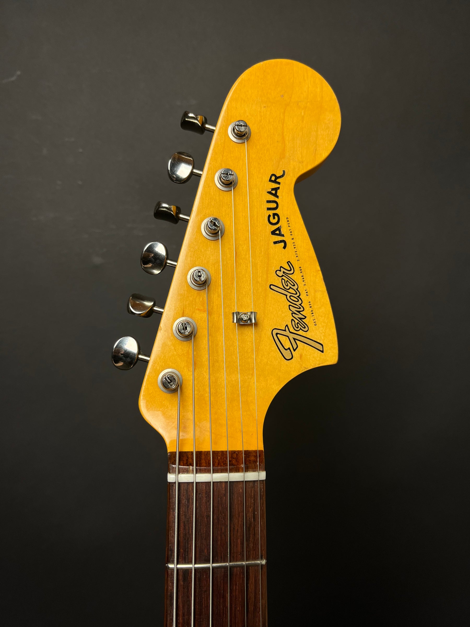Close-up of the guitar's amber-tinted headstock, showing six chrome tuners, a string tree, and the dark rosewood fretboard.