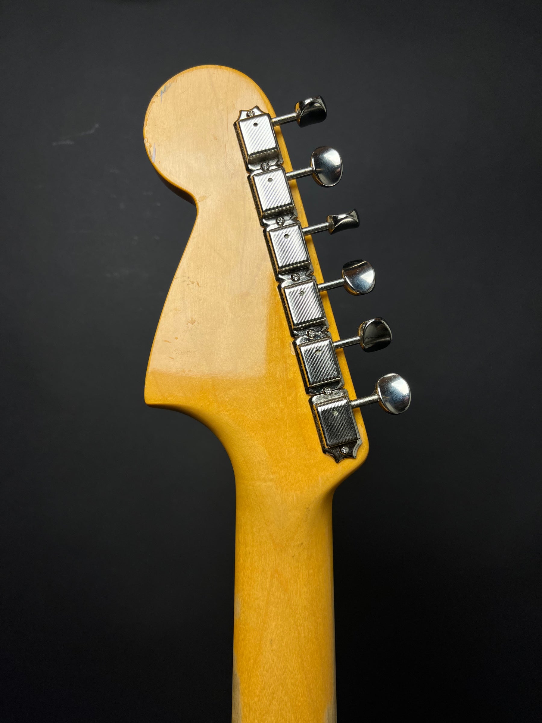 The guitar's headstock and upper neck, in a warm amber finish, show six chrome tuners with oval buttons and ribbed casings.