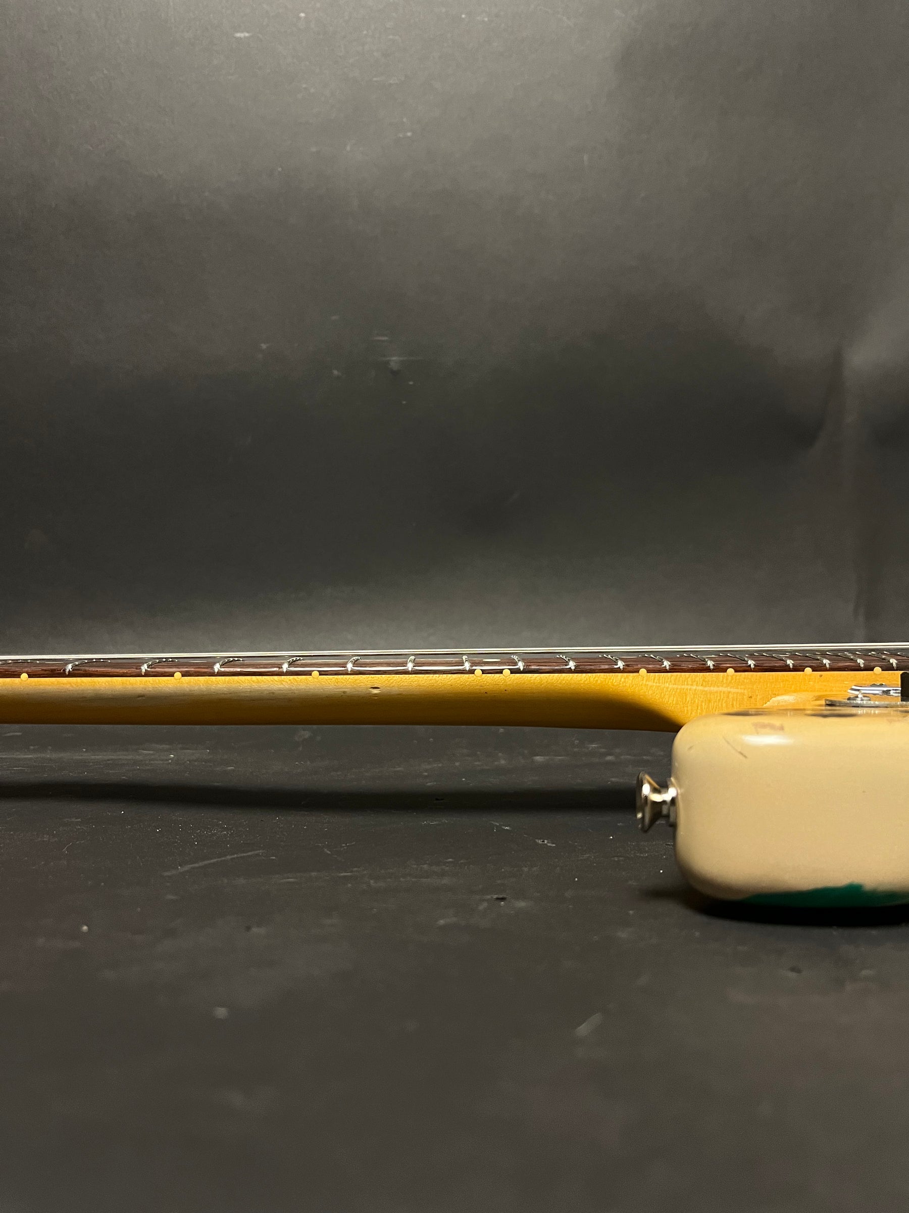 Side view of the guitar's neck and part of the body, showing a light-colored neck with a dark fretboard and cream body with green paint.