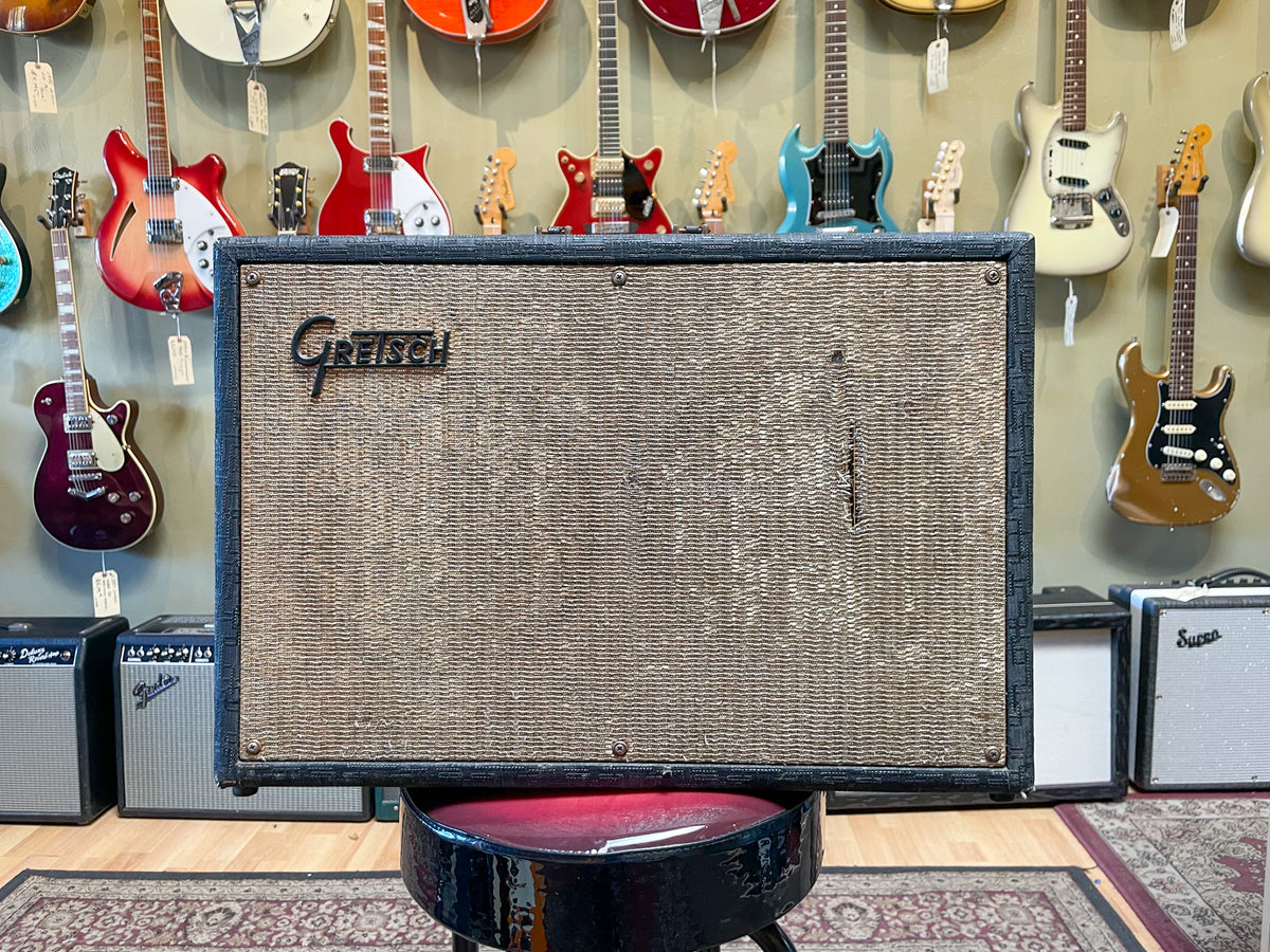 Front view of a vintage combo amp with a dark gray textured cabinet and a light brown woven grille cloth, showing wear.