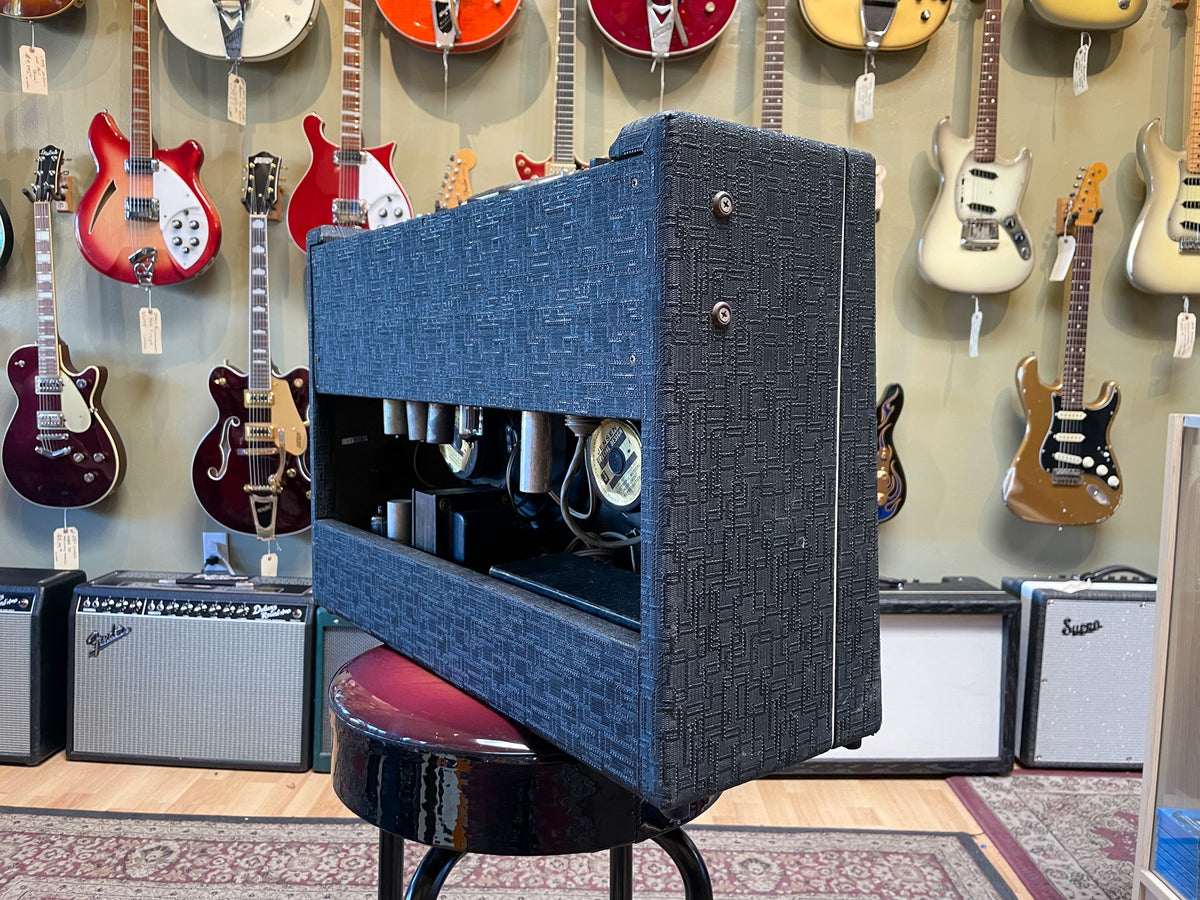 Dark gray textured combo amp, angled right, showing the side and open back with visible tubes and internal components.
