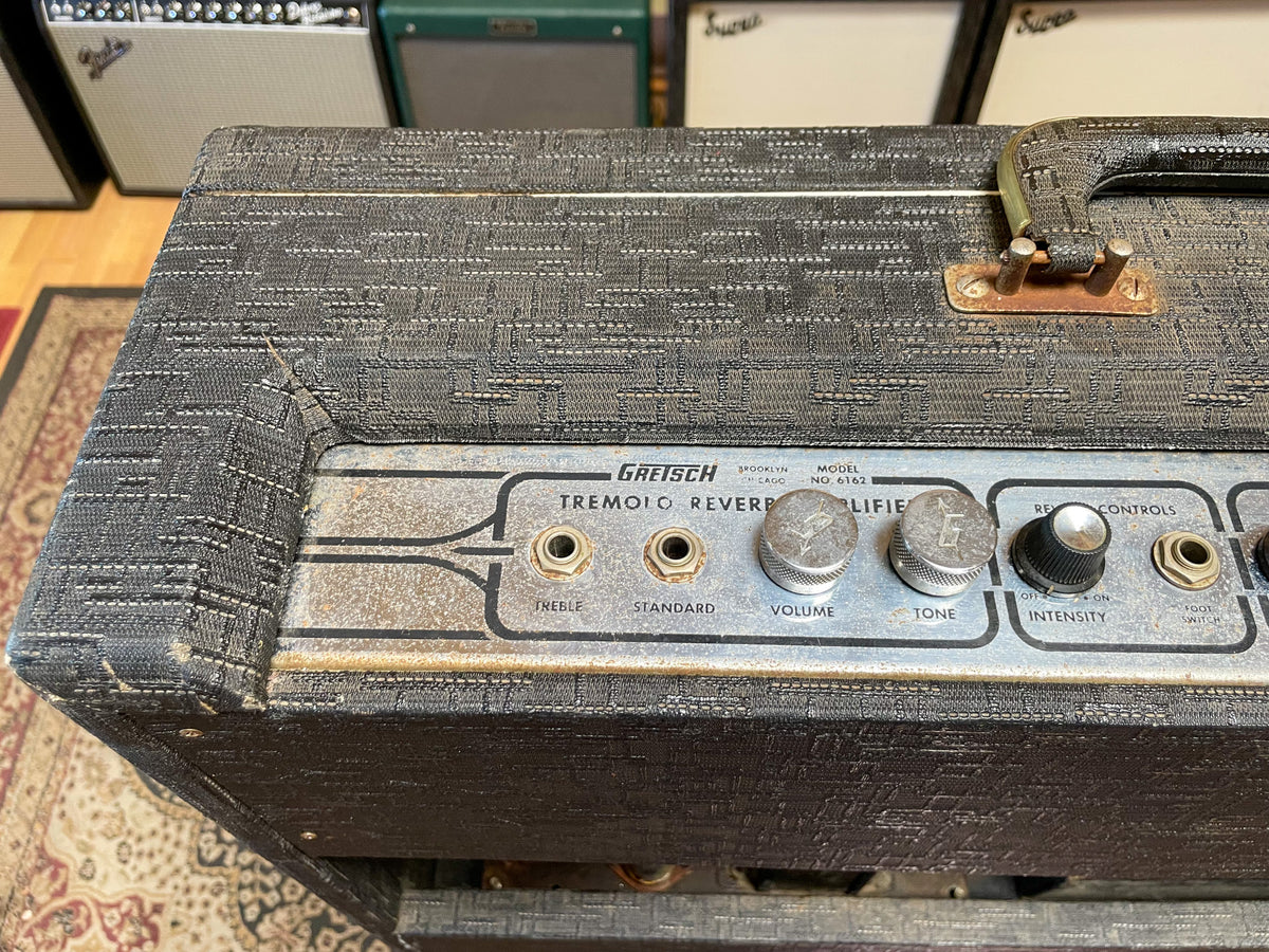 Top-down view of the amp's control panel, showing a worn black textured covering, tarnished metal faceplate, and four metal knobs.