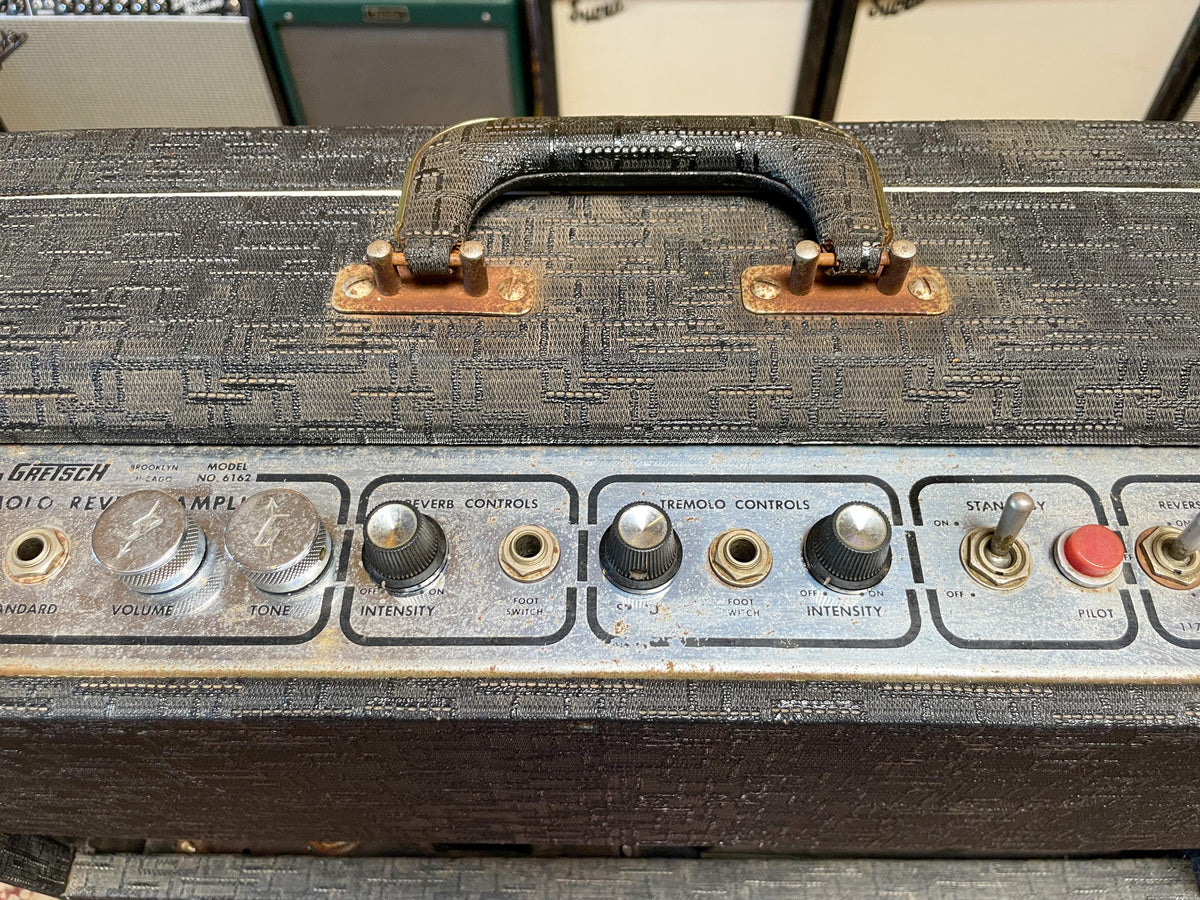 Top-down view of a black textured amp with a worn handle, showing the silver control panel with various knobs, switches, and jacks.