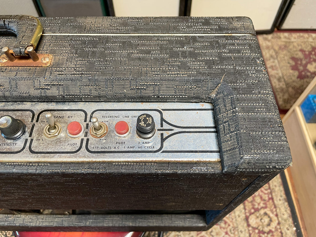 Close-up of the amp's top right, showing the worn black textured tolex, silver control panel with red pilot lights, and a brass handle.