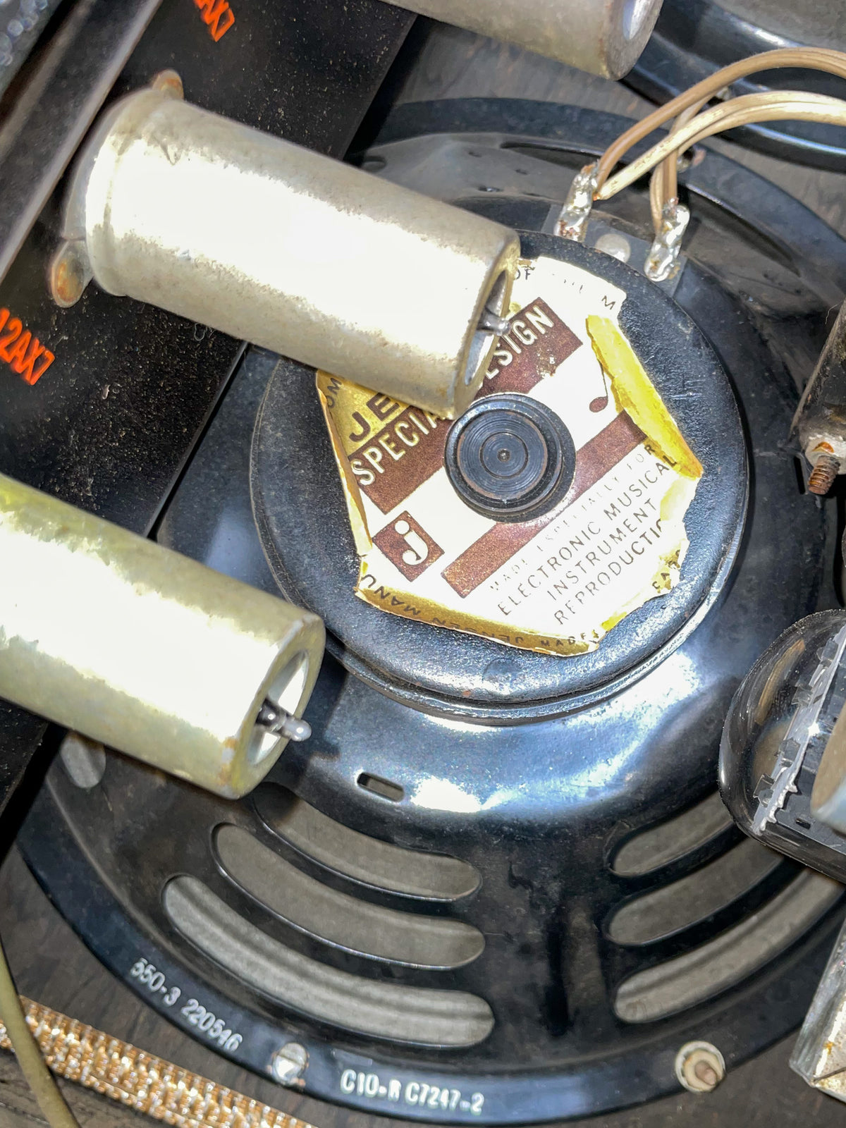 Close-up of the amp's internal speaker magnet and wiring, showing a worn paper label and two large, pale cylindrical capacitors.