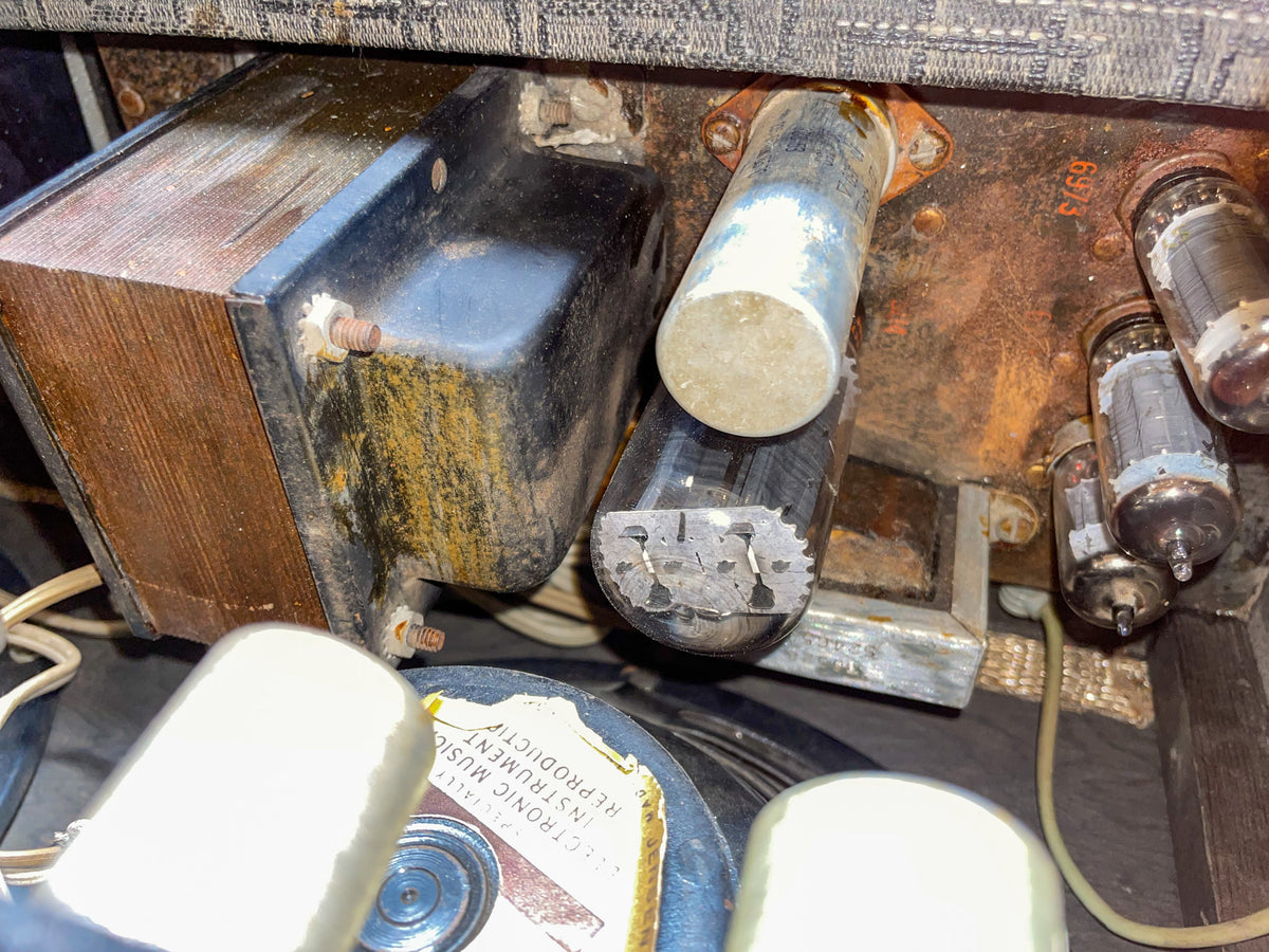 Close-up of the amp's rusty internal chassis, showing several vacuum tubes, a transformer, and a speaker cone with a partial label.