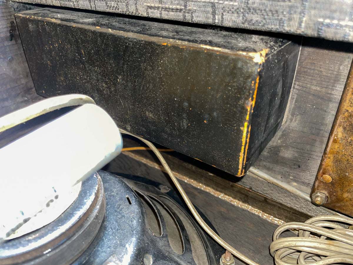 Close-up of the amp's interior, showing a black rectangular component with worn edges, a speaker magnet, and coiled wires.