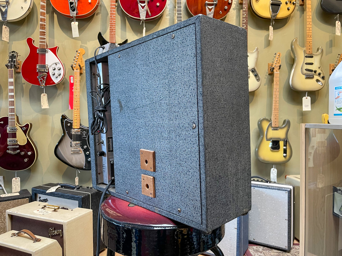 The dark gray textured amp is angled right, showing its side and back, with two square wooden blocks on the back.