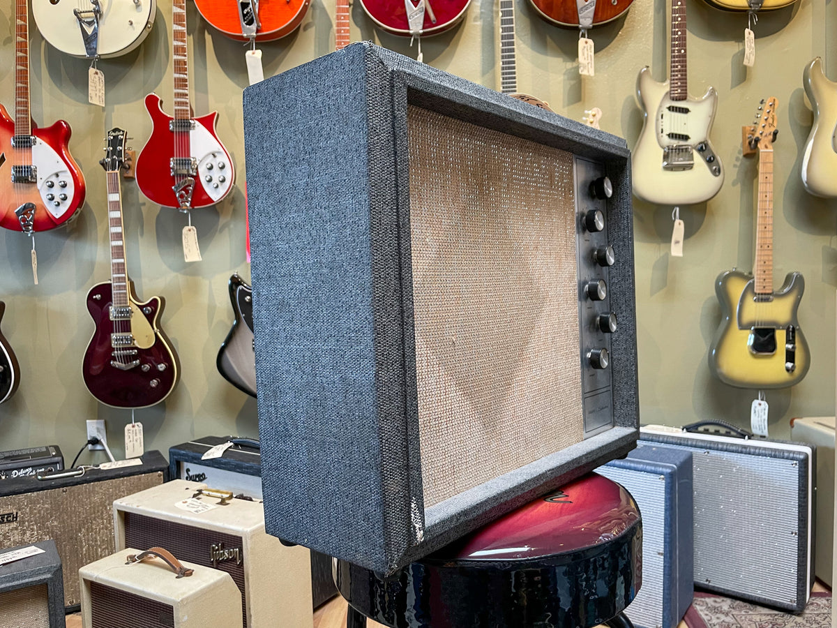 The vintage combo amp is angled right, showing its dark gray tweed cabinet, tan grille cloth, and five black control knobs.