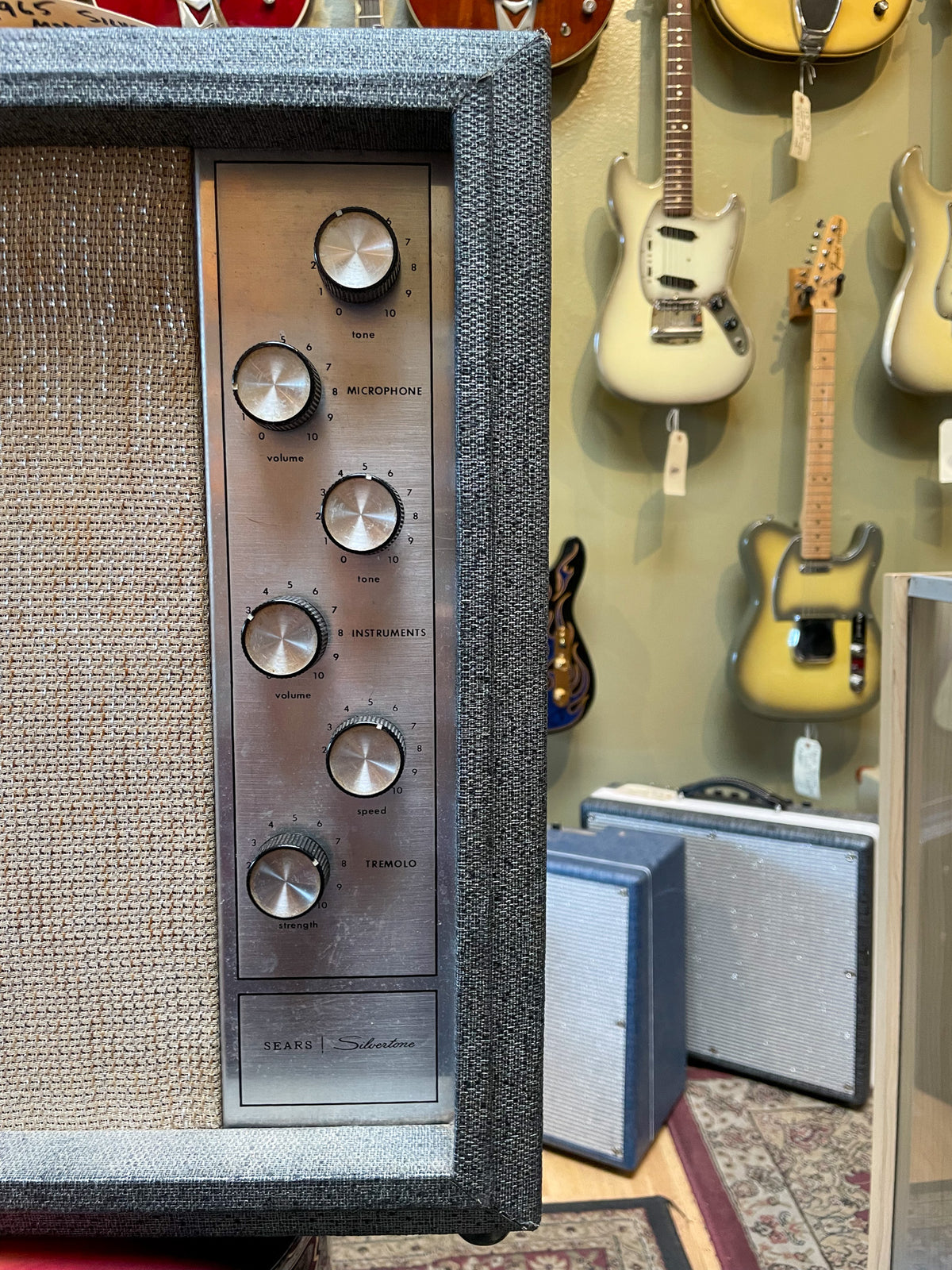 The amp's gray tweed cabinet and tan grille cloth frame a brushed metal control panel with six chrome knobs and wear.