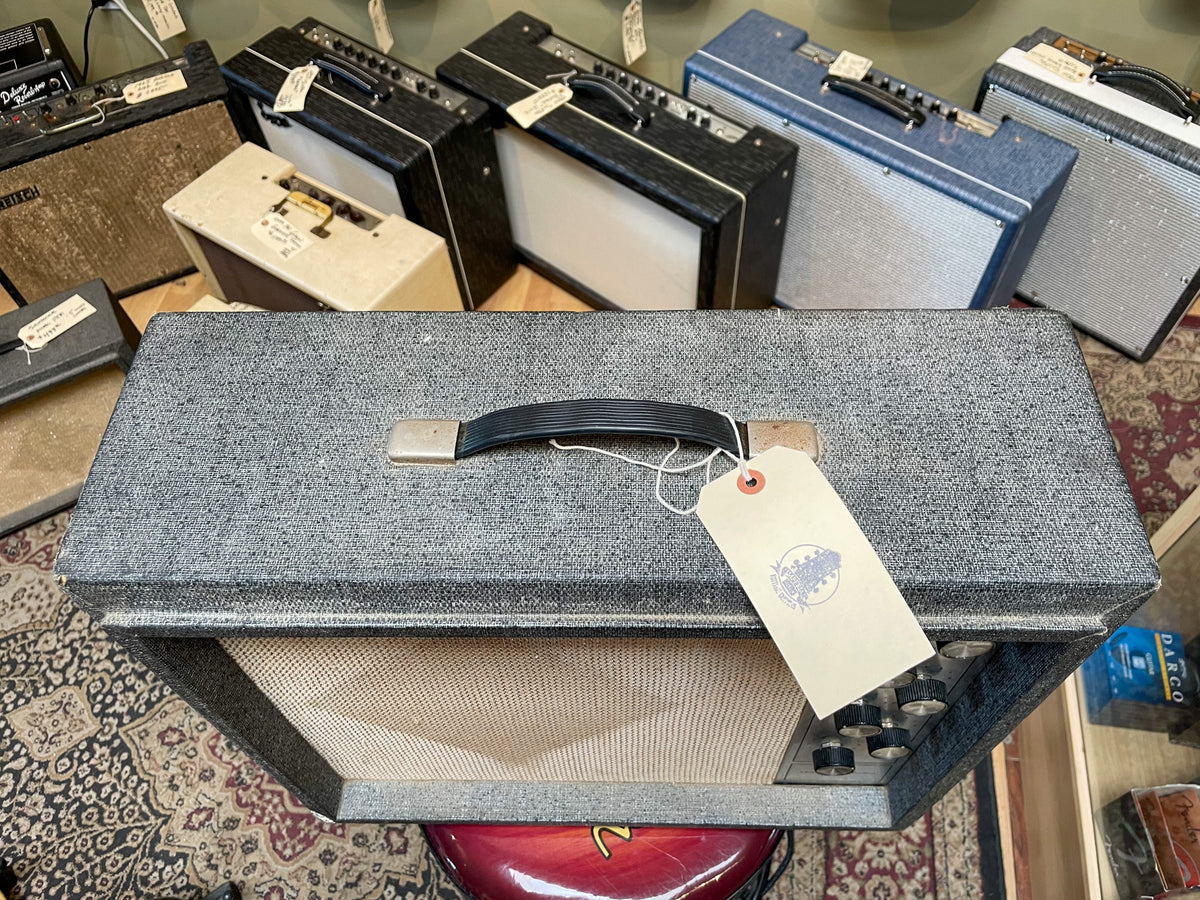 Top-down view of a gray tweed combo amp with a black handle, light grill cloth, and four black control knobs.