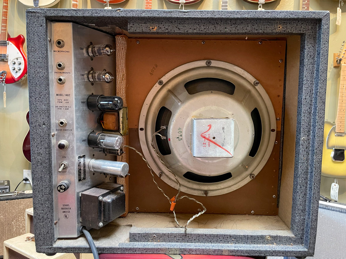 Rear view of the open-back combo amp, revealing a large speaker, several vacuum tubes, and the silver control panel with inputs and switches.