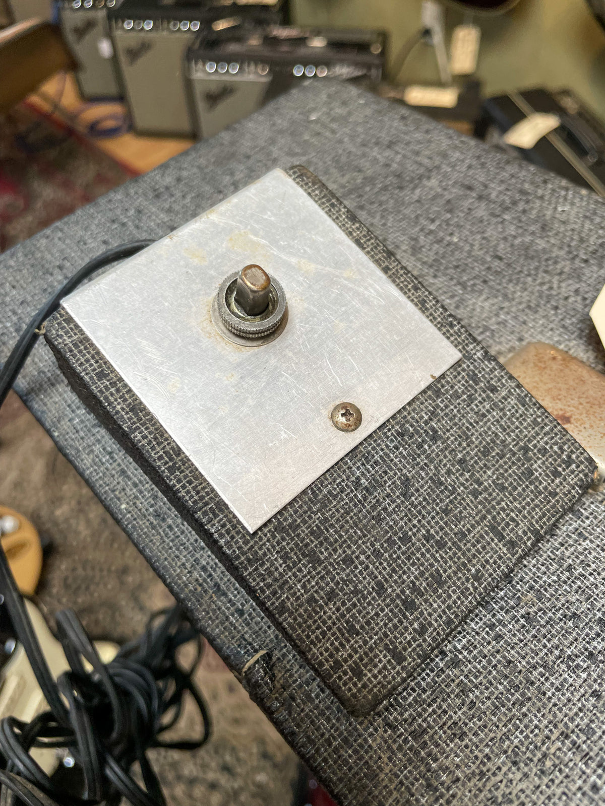 Close-up of the amp's dark gray textured footswitch with a brushed metal plate, a single worn metal toggle switch, and a rusty screw.