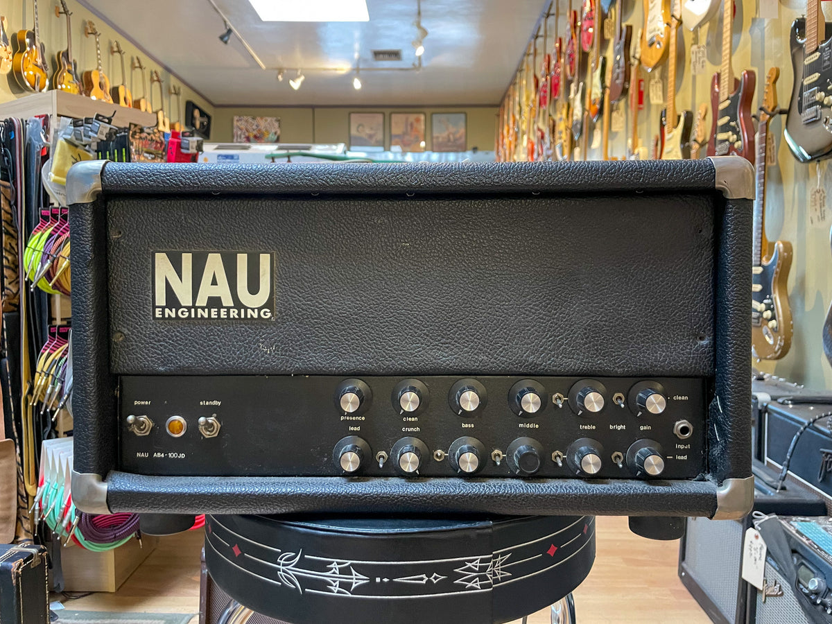 Black textured amplifier head with a silver faceplate, featuring 15 silver-capped black knobs, two toggle switches, and a single amber indicator light.