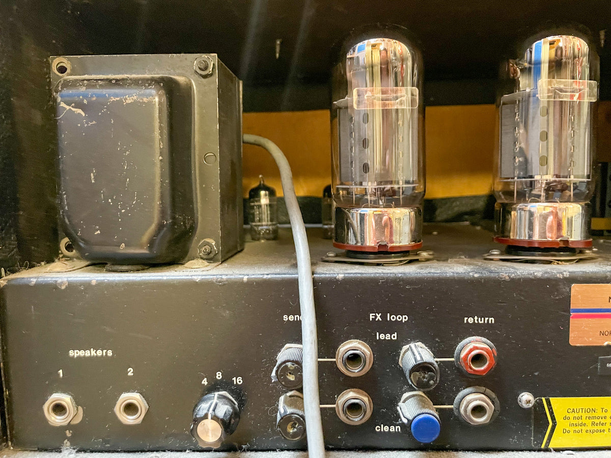 Rear view of the dusty black amplifier head, showing two large vacuum tubes, speaker outputs, and FX loop jacks with worn knobs.