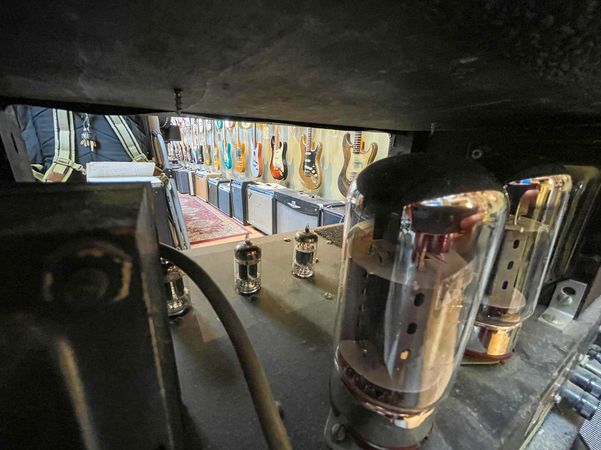 Looking down into the amp head, three large glowing vacuum tubes are visible, with smaller tubes and wiring further back.