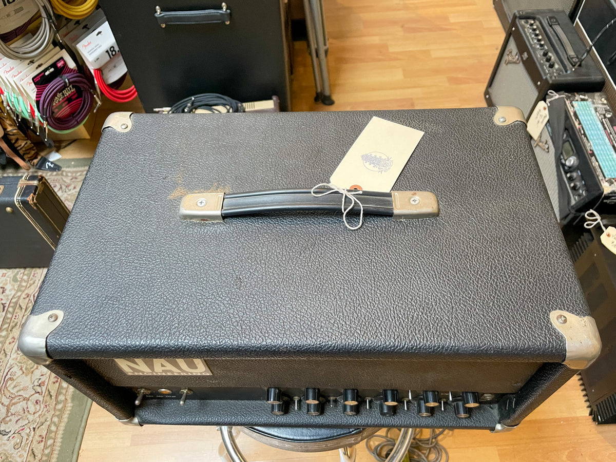 Overhead view of a black textured amp head with a top handle, metal corner protectors, and a row of black knobs on the front panel.