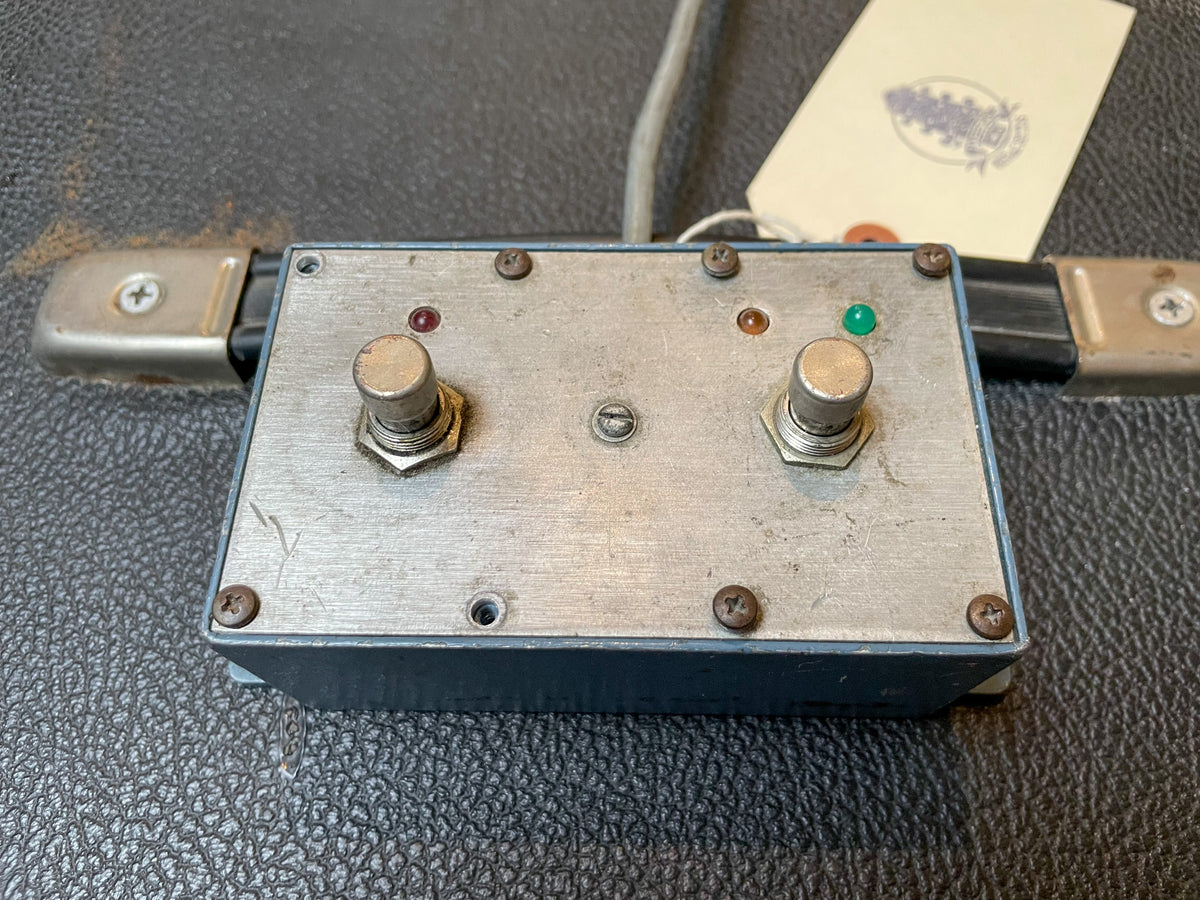 Top-down view of a grey metal footswitch with two silver stomp buttons, a red and a green indicator light, and visible scratches.