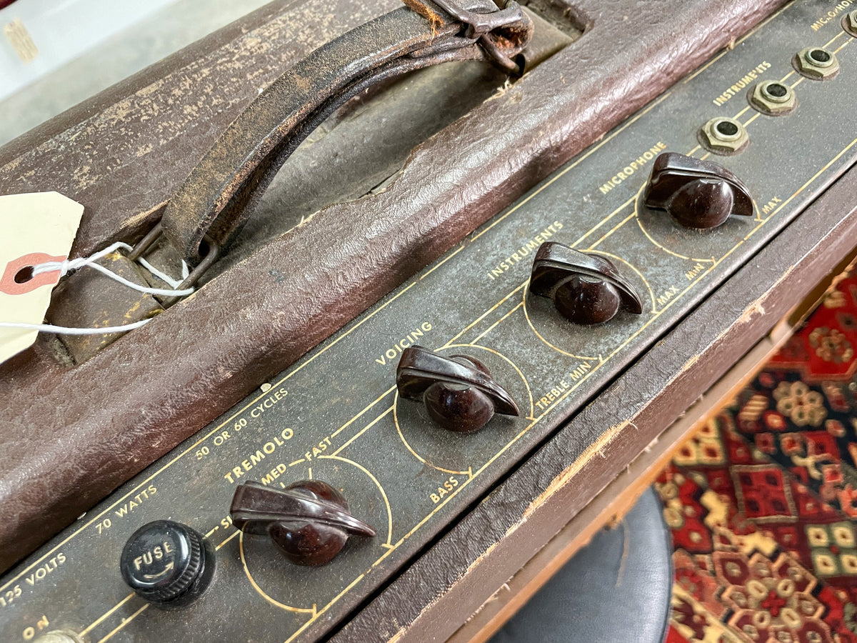 Close-up of a vintage Gibson GA-40 amp's control panel, showing brown knobs, a fuse cap, and a worn leather handle.