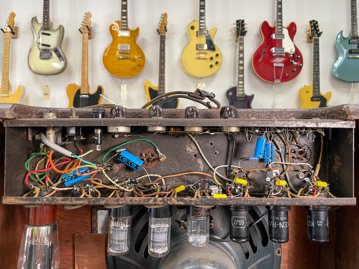 Top-down view of the amp's exposed chassis, revealing internal wiring, tubes, and various blue and yellow capacitors.