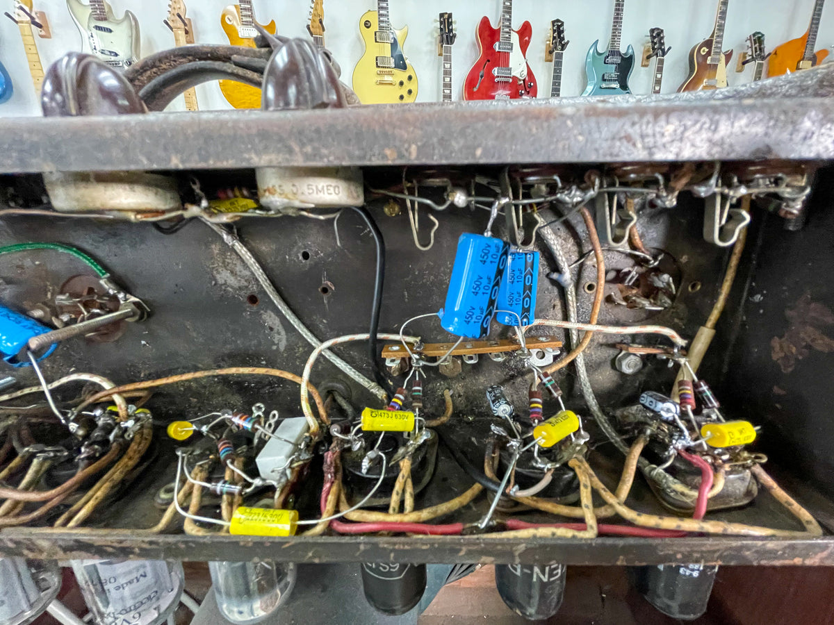 A top-down view of the amp's dusty, dark brown chassis, revealing a dense network of wires, resistors, and blue and yellow capacitors.