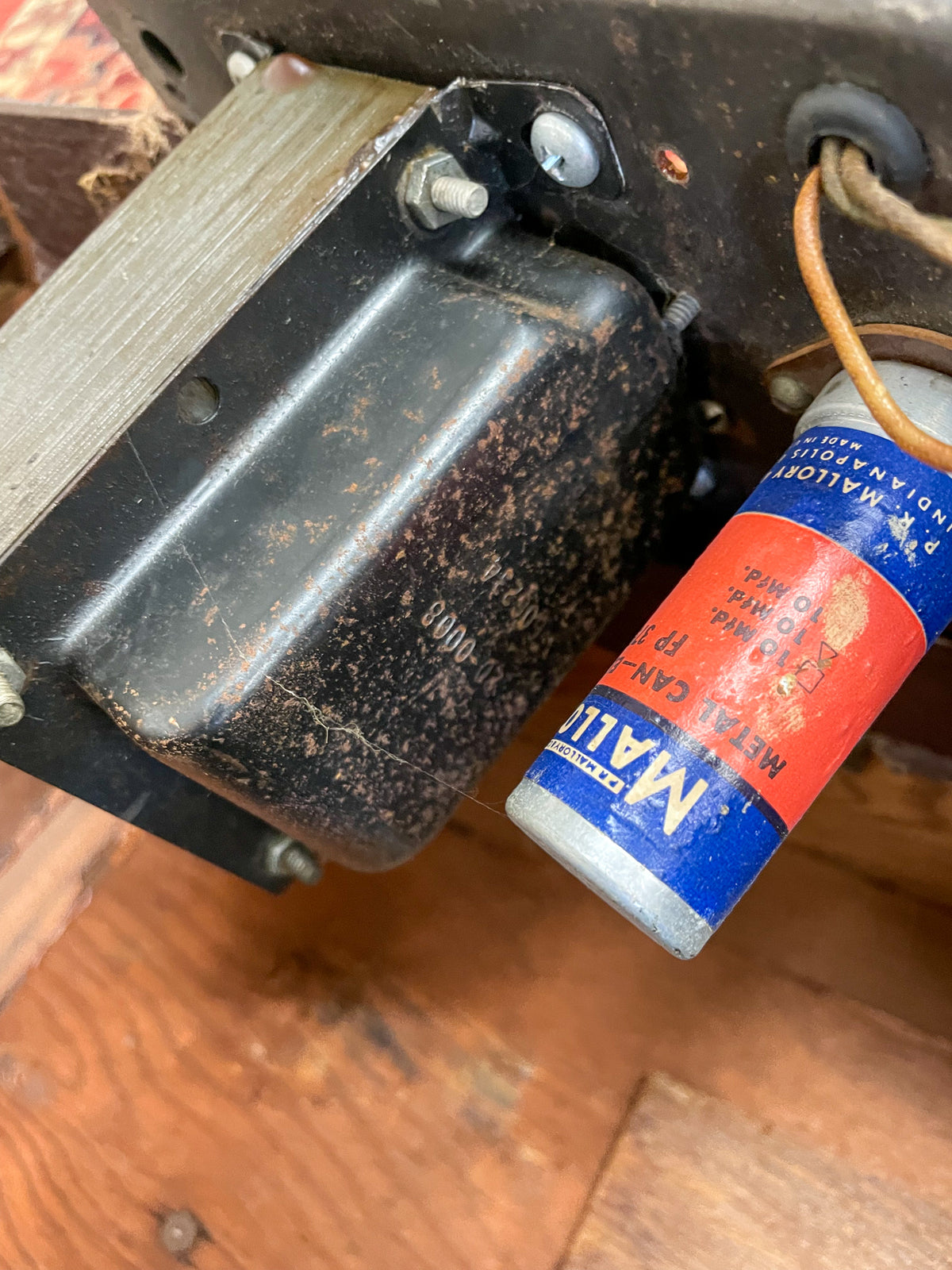 Close-up of the amp's rusty black transformer and a red and blue capacitor, with wires and a wooden surface visible.