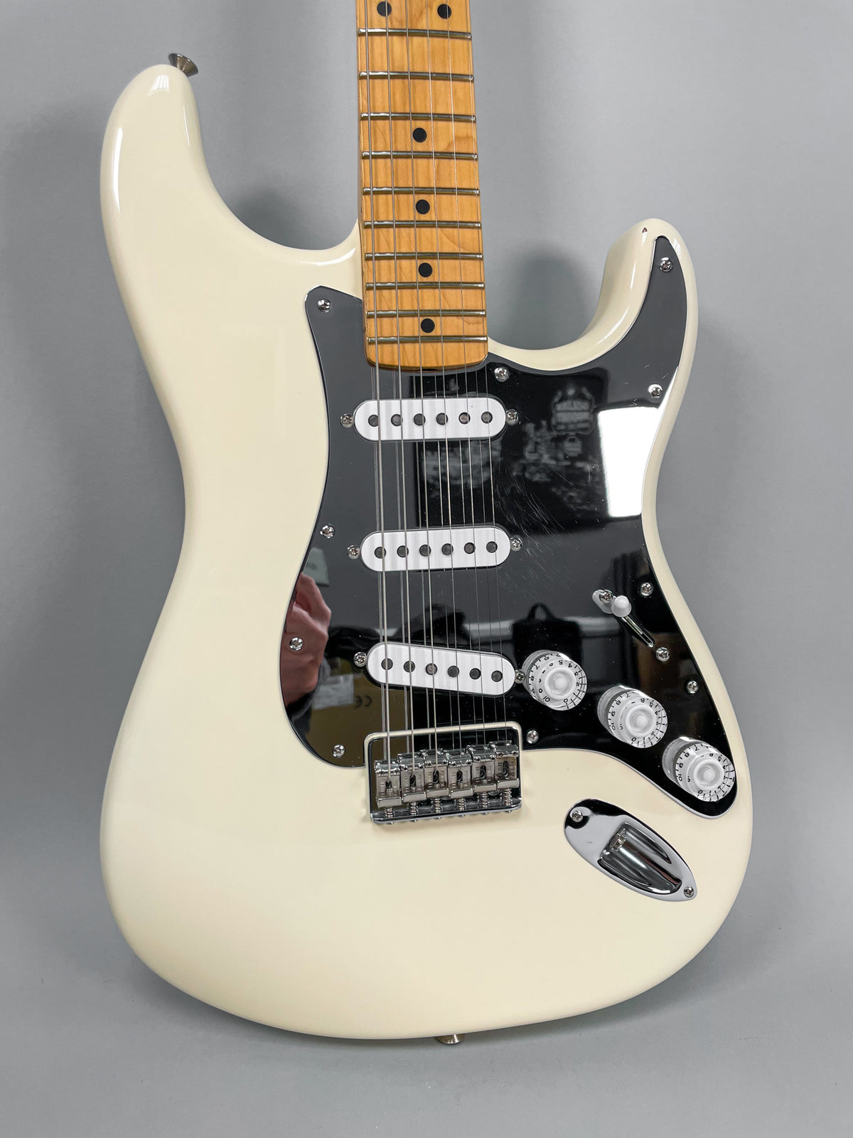 An Olympic White Stratocaster, angled to the right, shows its black pickguard with three single-coil pickups and three white control knobs.