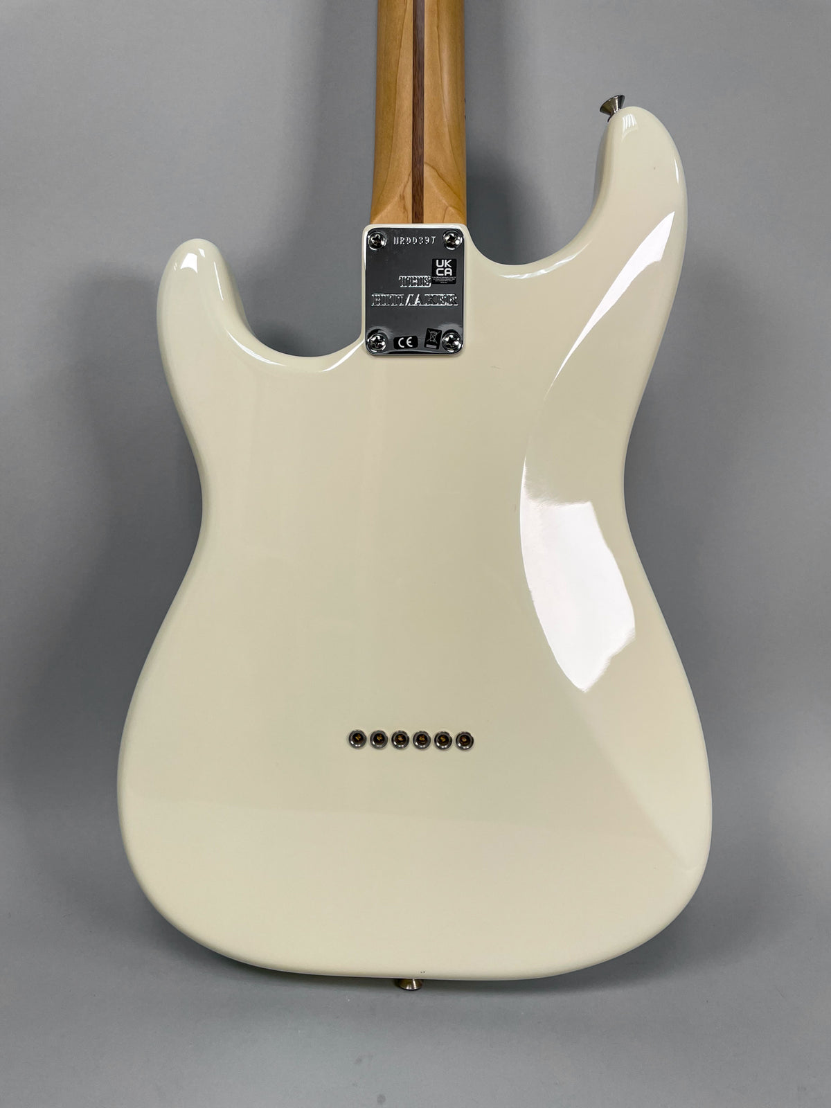 Rear view of an Olympic White Stratocaster body with a glossy finish, showing the neck plate, string-through-body ferrules, and strap button.