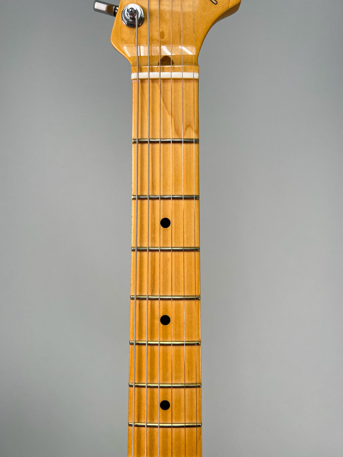 Close-up of the maple fretboard and headstock, showing black dot inlays and chrome tuners on a light wood finish.