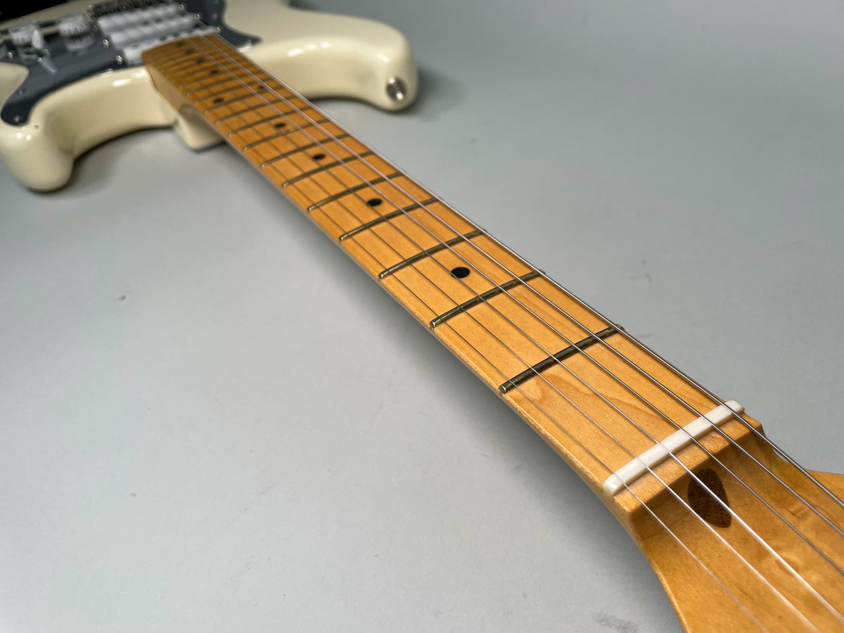 The Olympic White Stratocaster's maple fretboard with black dot inlays and a white nut is viewed from the headstock towards the body.