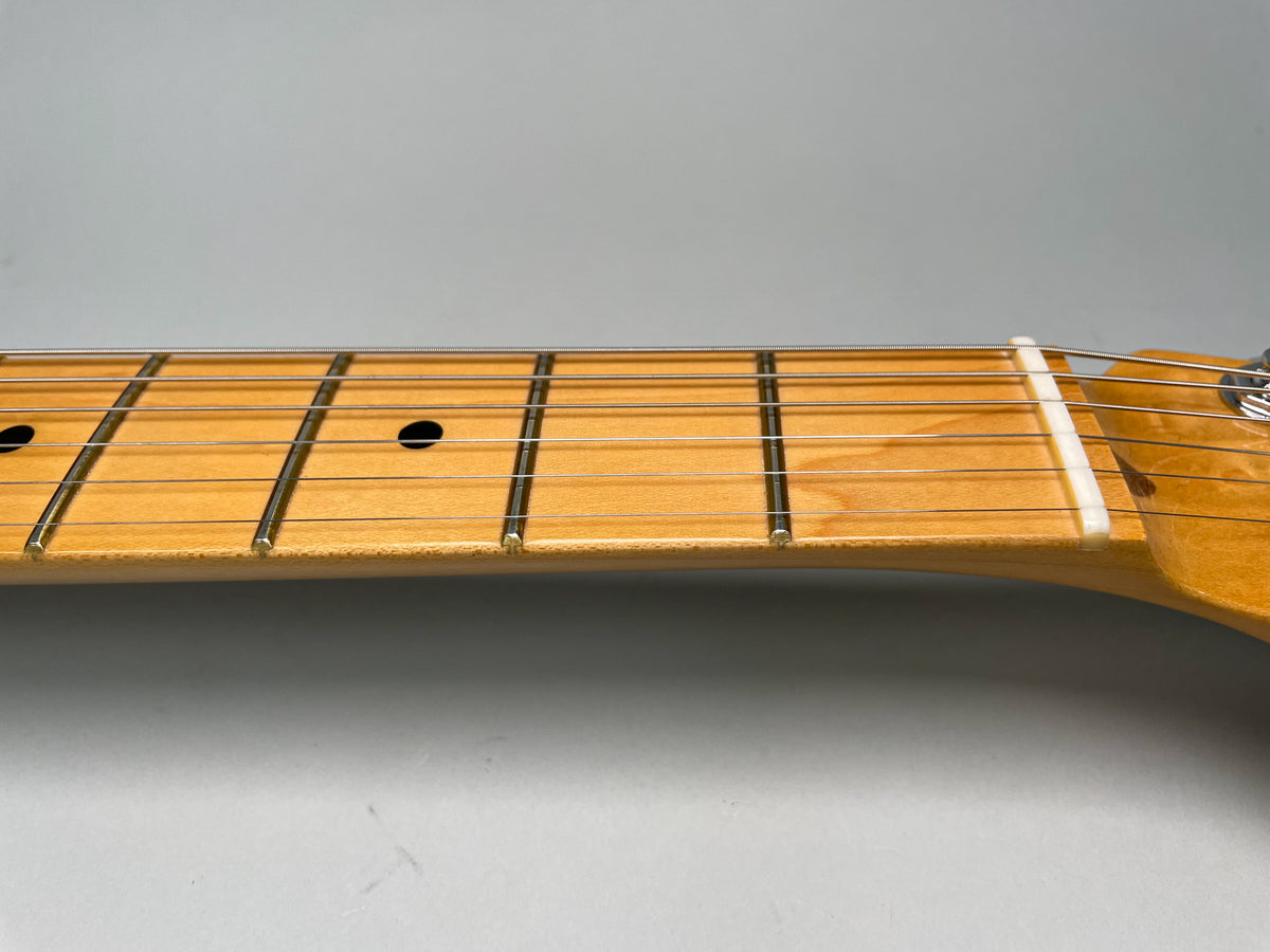 Close-up of the maple fretboard and frets, showing the nut and the first few black dot inlays.