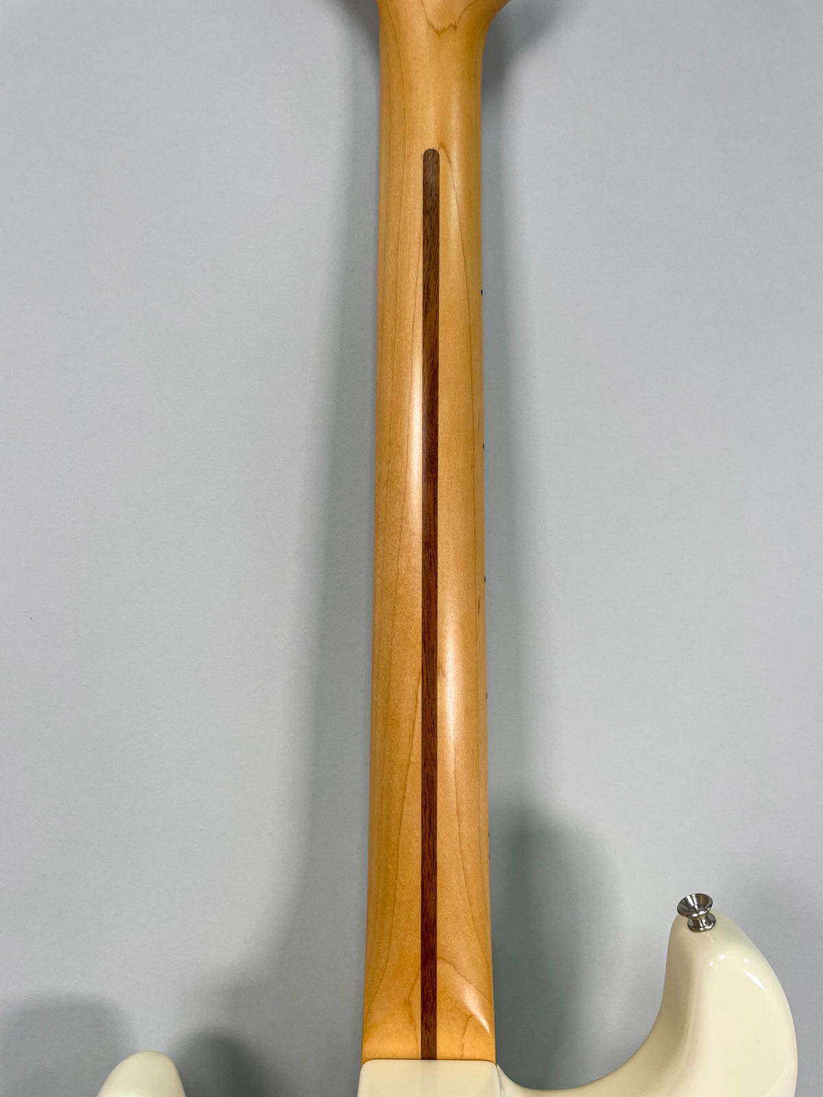 The guitar's light maple neck, with a dark wood skunk stripe, is viewed from the back, with a white body visible at the bottom.