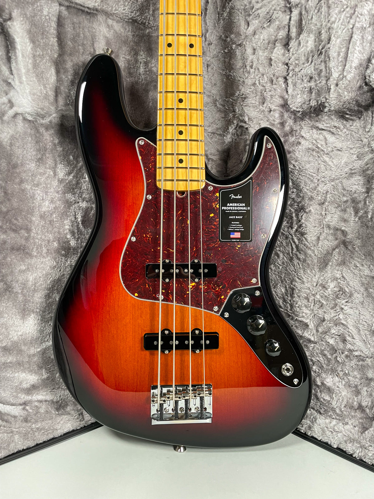 The sunburst bass guitar is angled slightly right, showing its glossy finish, tortoiseshell pickguard, and maple fretboard.