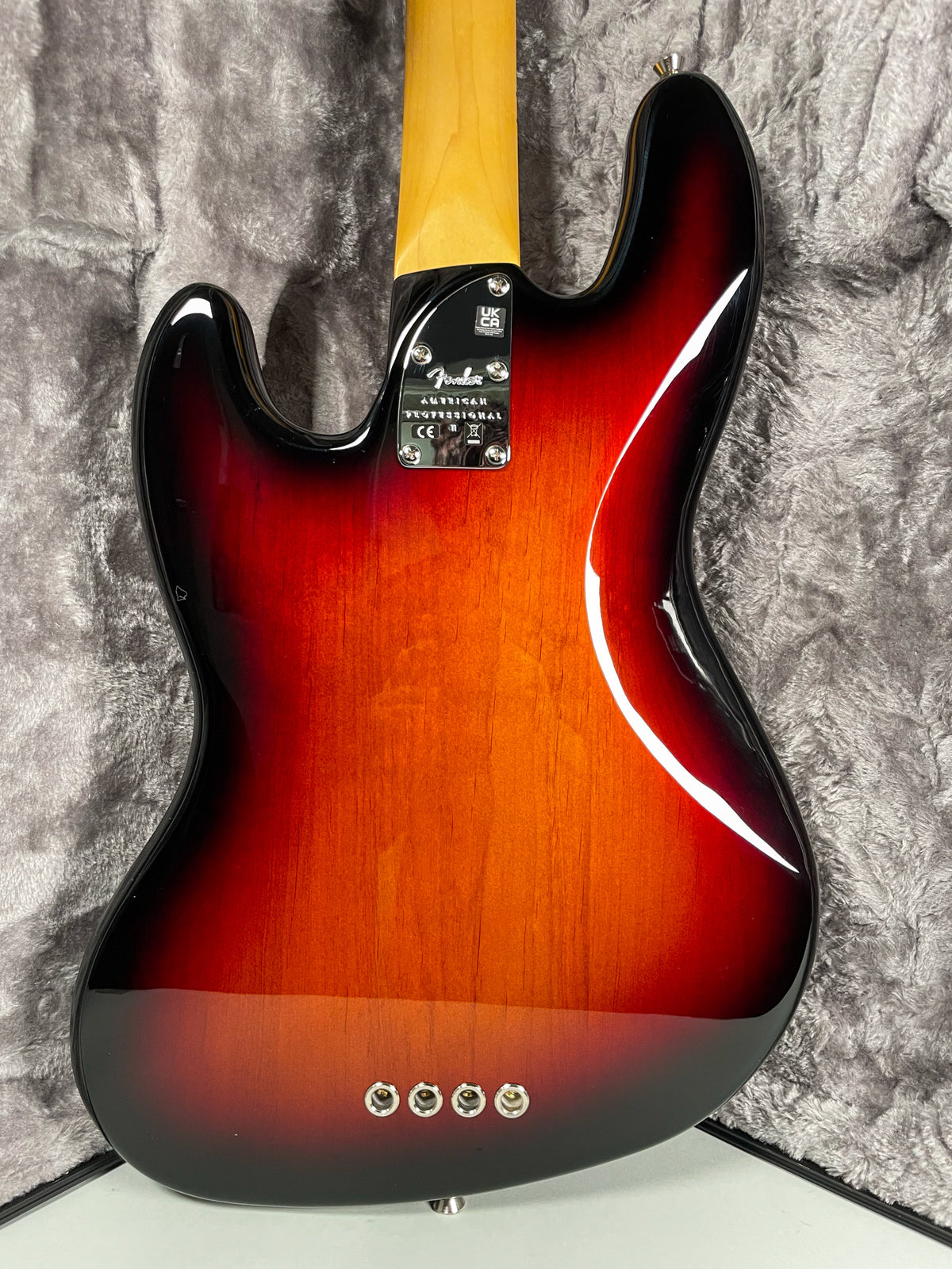 The bass's glossy sunburst back, with a light wood center fading to dark edges, shows a chrome neck plate and four string ferrules.