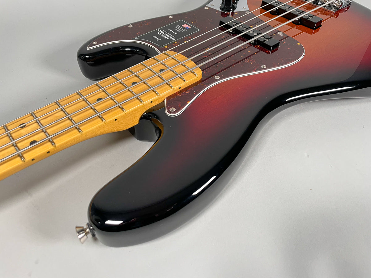 Upper body of a sunburst bass guitar, showing the glossy black lower bout, reddish-brown mid-section, and a light maple neck.