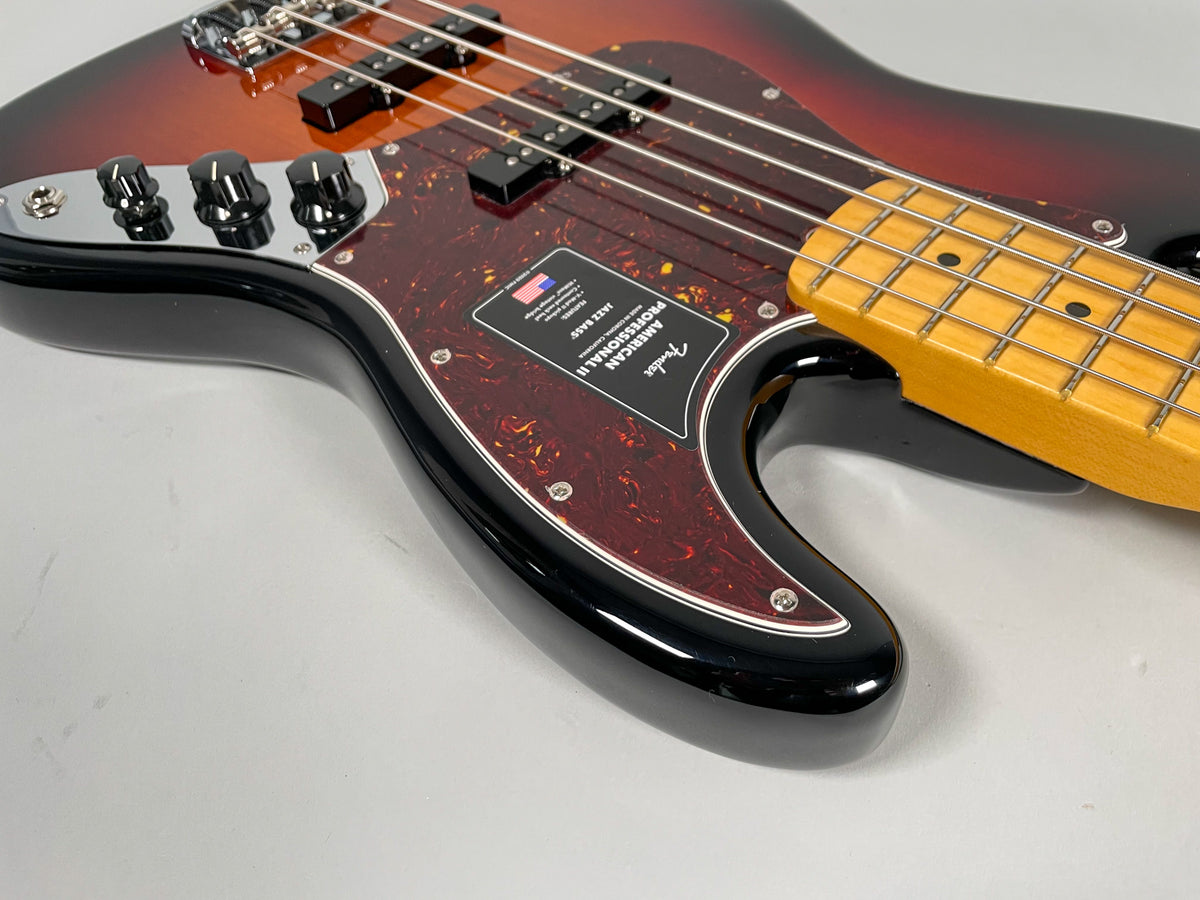 Close-up of a sunburst Jazz Bass, showing the lower body, dark tortoiseshell pickguard, black control knobs, and maple fretboard.
