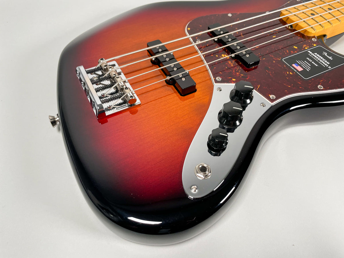 Close-up of a sunburst bass guitar body, showing the chrome bridge, two black pickups on a tortoiseshell pickguard, and three black control knobs.
