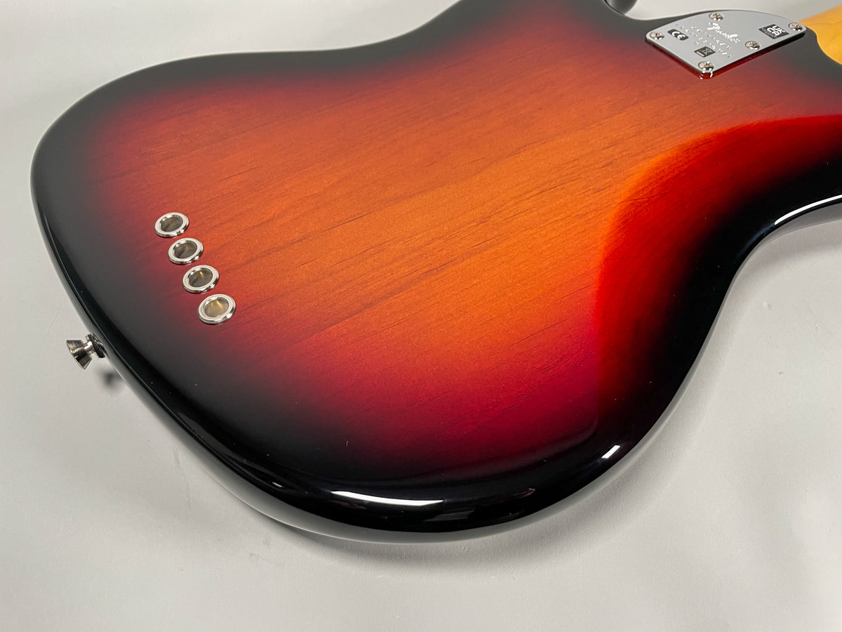 Close-up of the bass guitar's glossy sunburst body from the back, showing four chrome string ferrules and the neck plate.