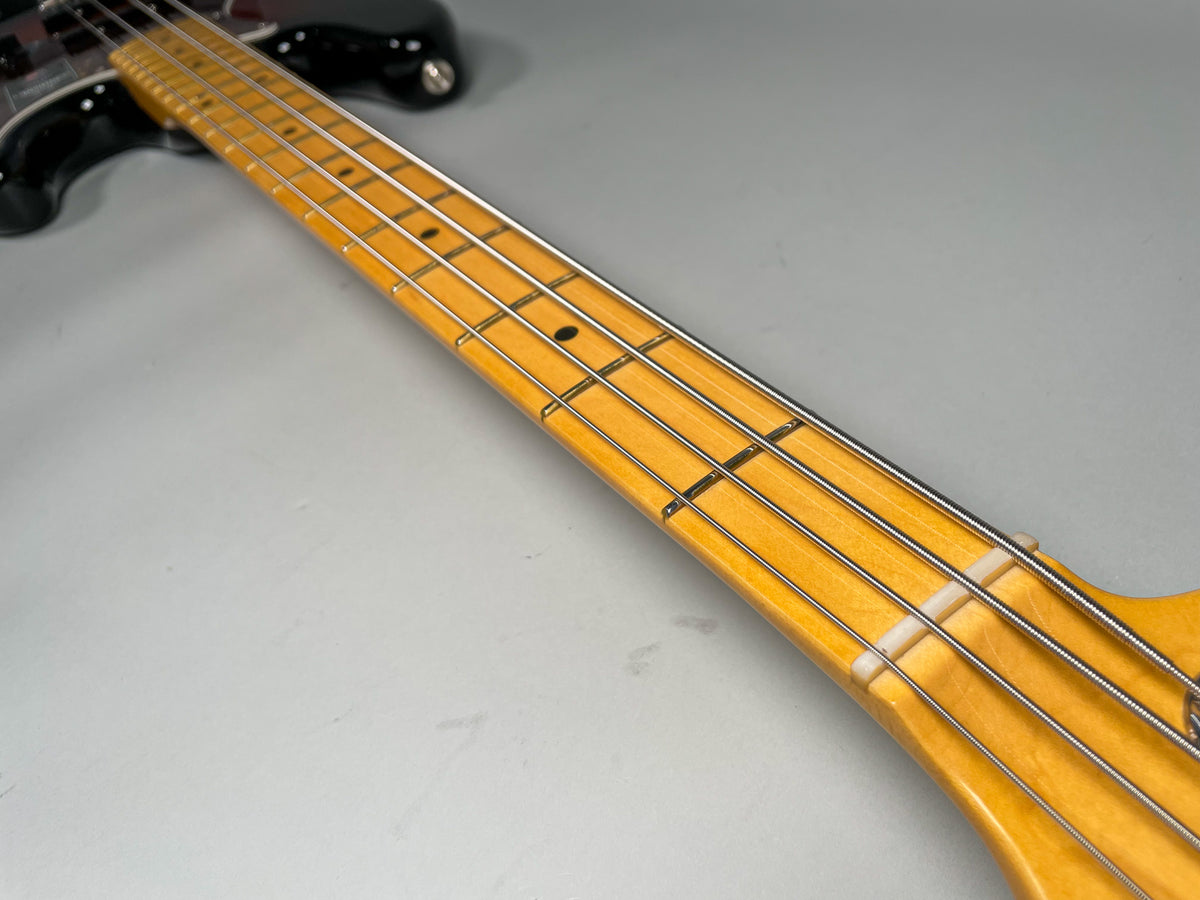 The bass guitar's maple neck and fretboard, with black dot inlays and a white nut, extends diagonally from the sunburst body.