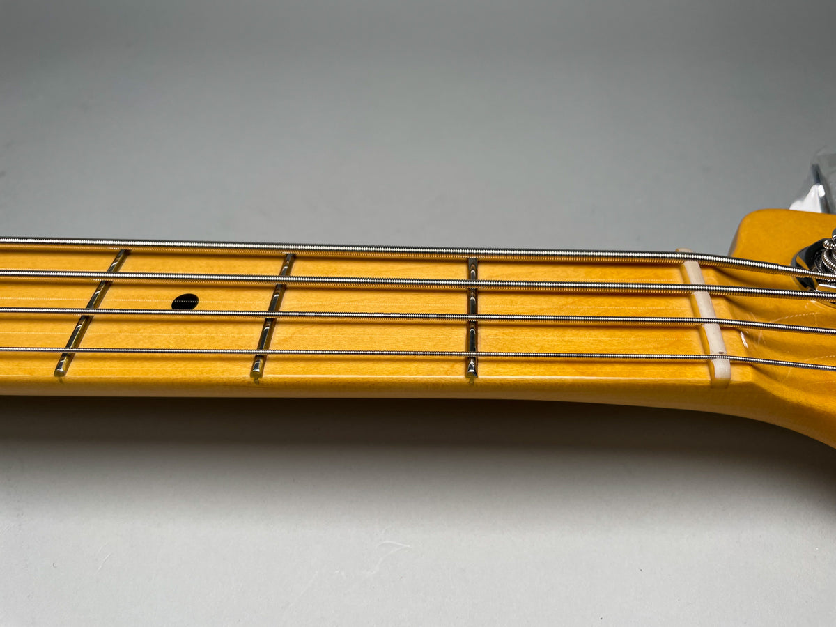 Close-up of the bass guitar's maple fretboard, showing the first five frets, dot inlays, and the white nut.